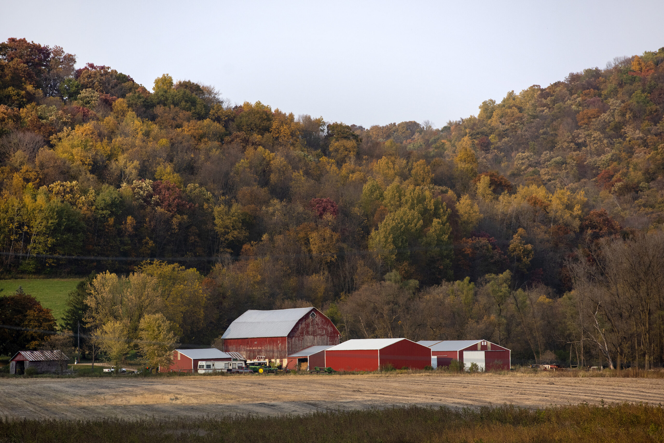 Hills with fall colors surround a red barn