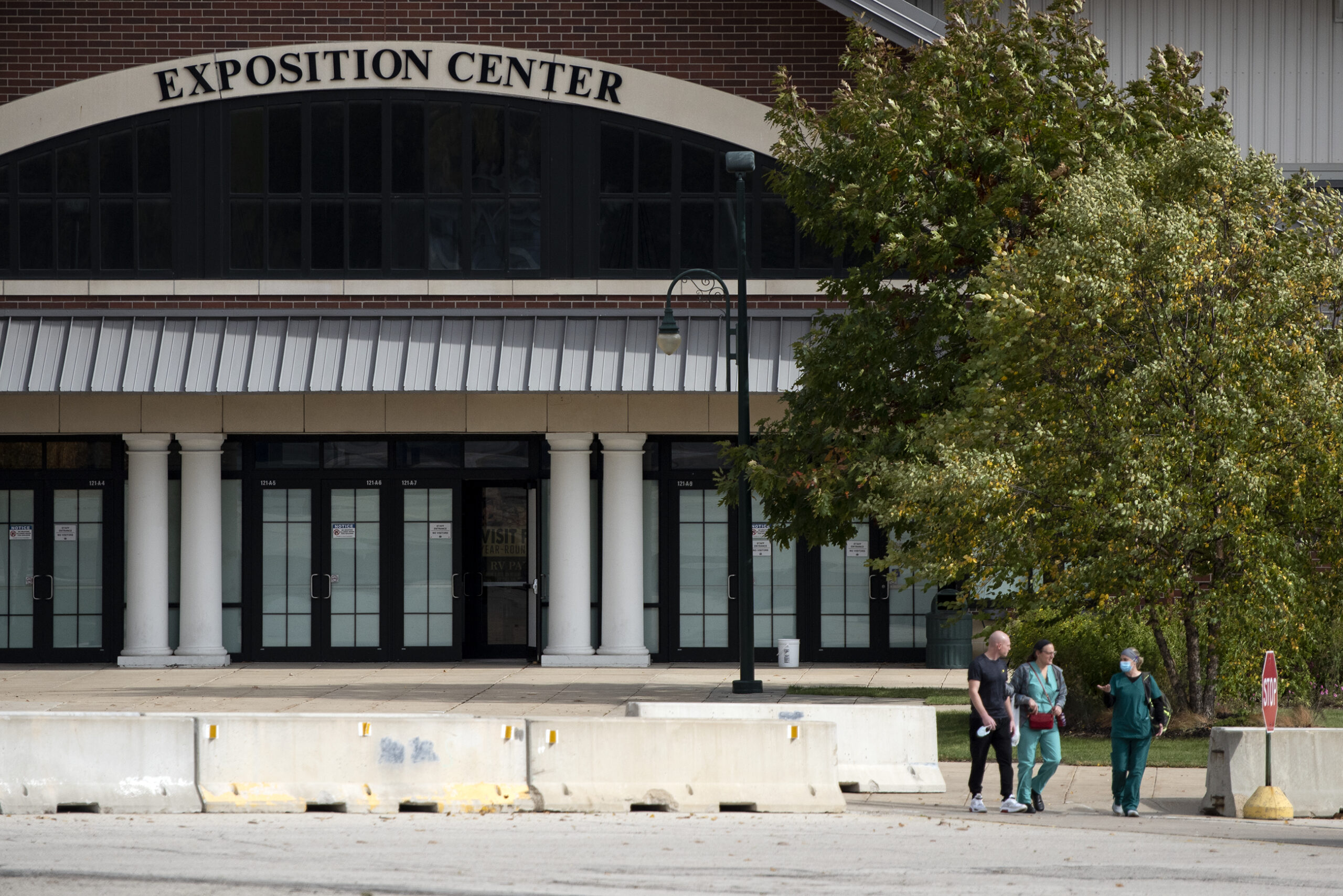 three people in scrubs walk through a parking lot in front of the Exposition Center