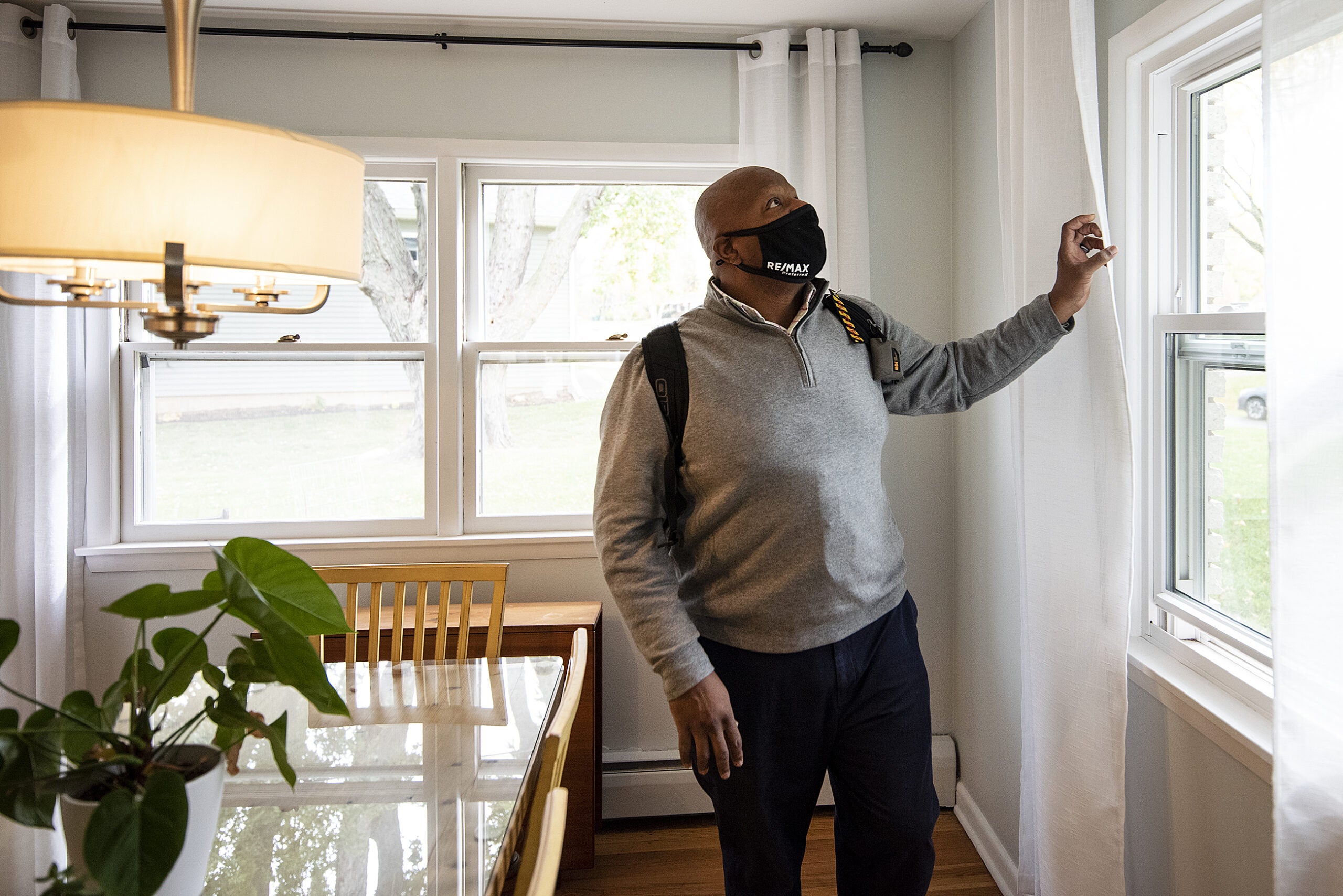 A man pulls on a white curtain to let in sunlight
