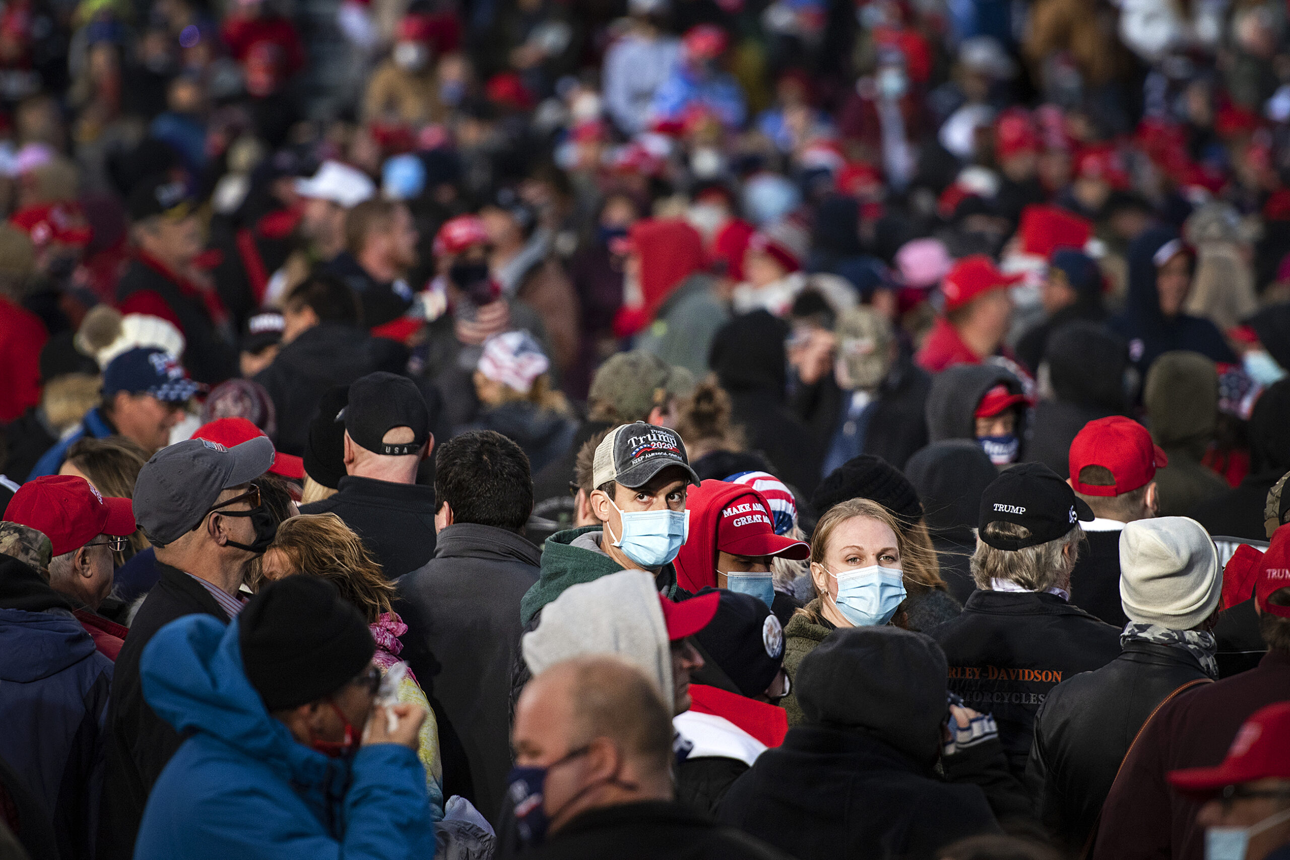 A man in a Trump hat and face mask is surrounded by fellow Trump supporters