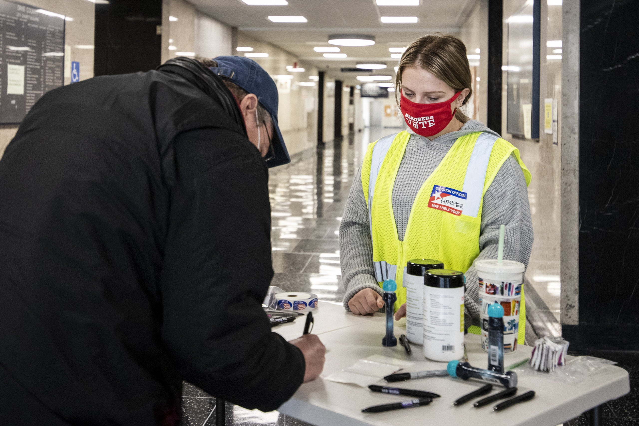 a poll worker in a mask watches as a voter completes his ballot