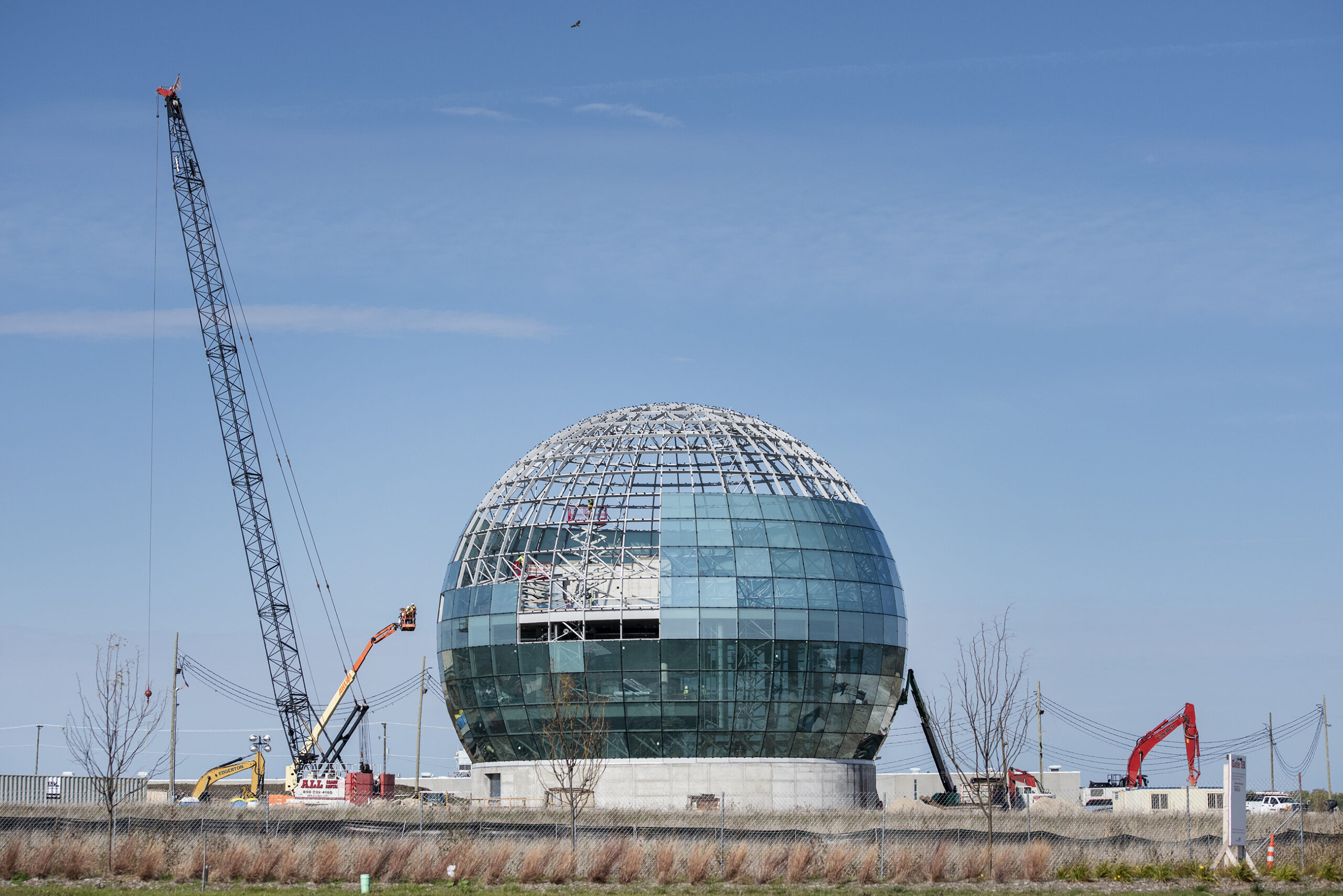 Cranes surround a large globe under a blue sky