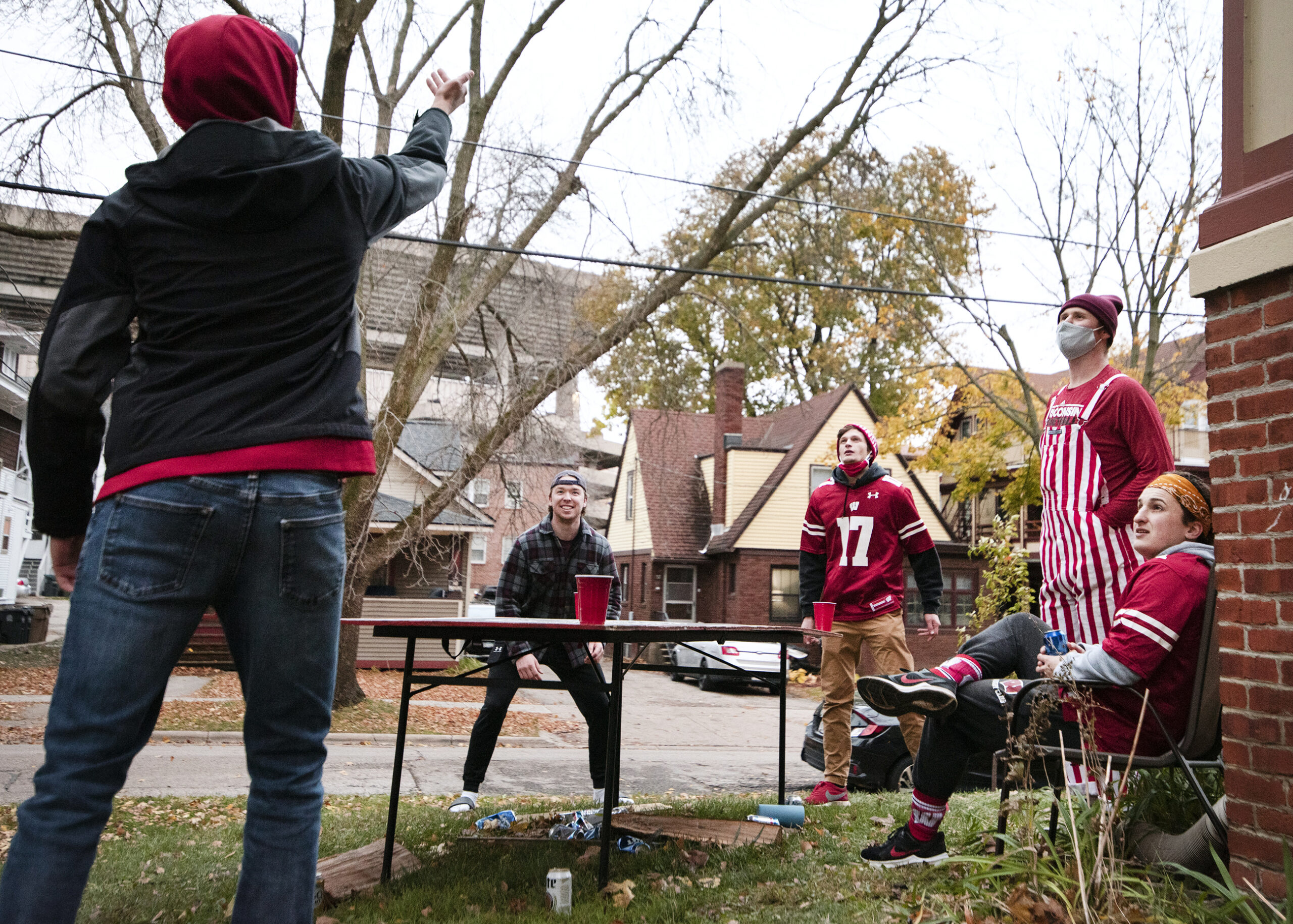 five students play a drinking game in a yard while wearing badgers gear