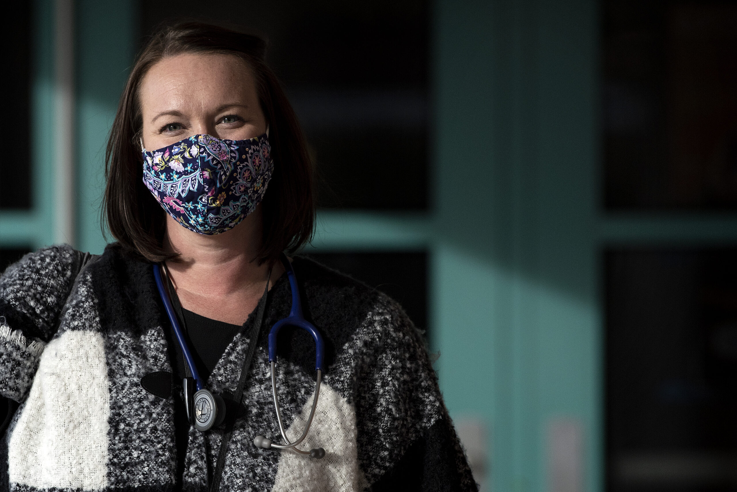 A woman in a face mask wears a stethoscope around her neck