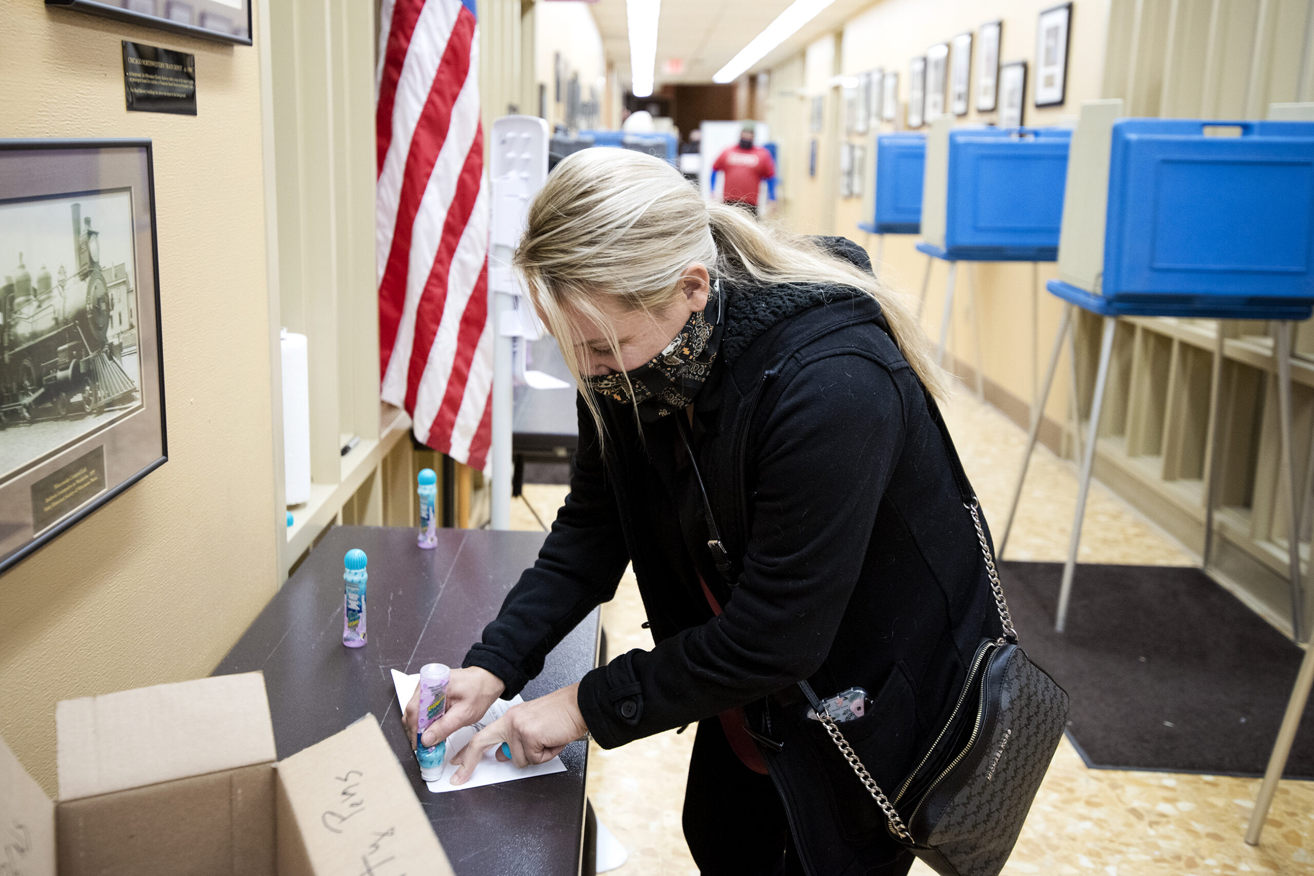 A woman uses glue to seal her ballot in an envelope. Voting booths can be seen in the background.