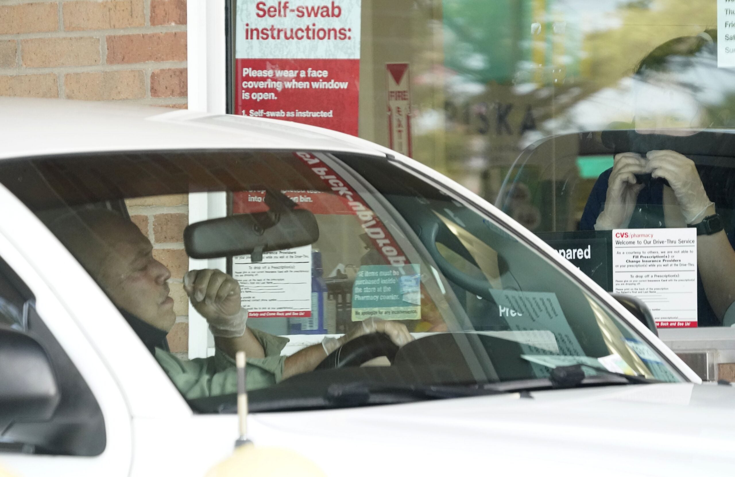 Pharmacy workers give instruction on how to administer a self COVID-19 nasal swab test at a drive-up CVS pharmacy