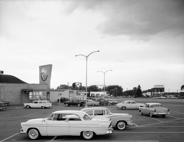 A  parking lot view of a strip mall in black and white featuring a Piggly Wiggly logo sign.