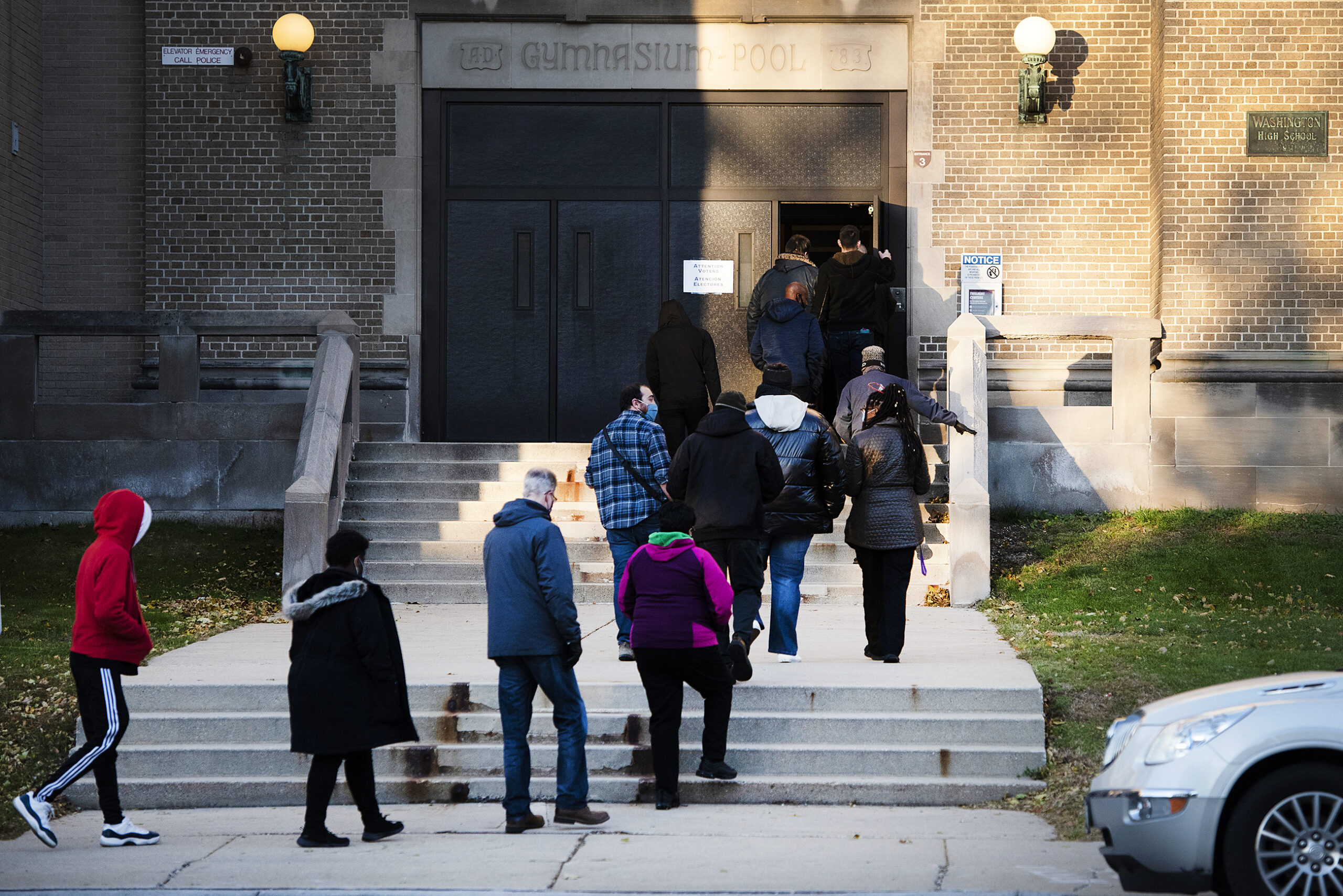 about thirteen voters in a line enter doors to a school as polls open