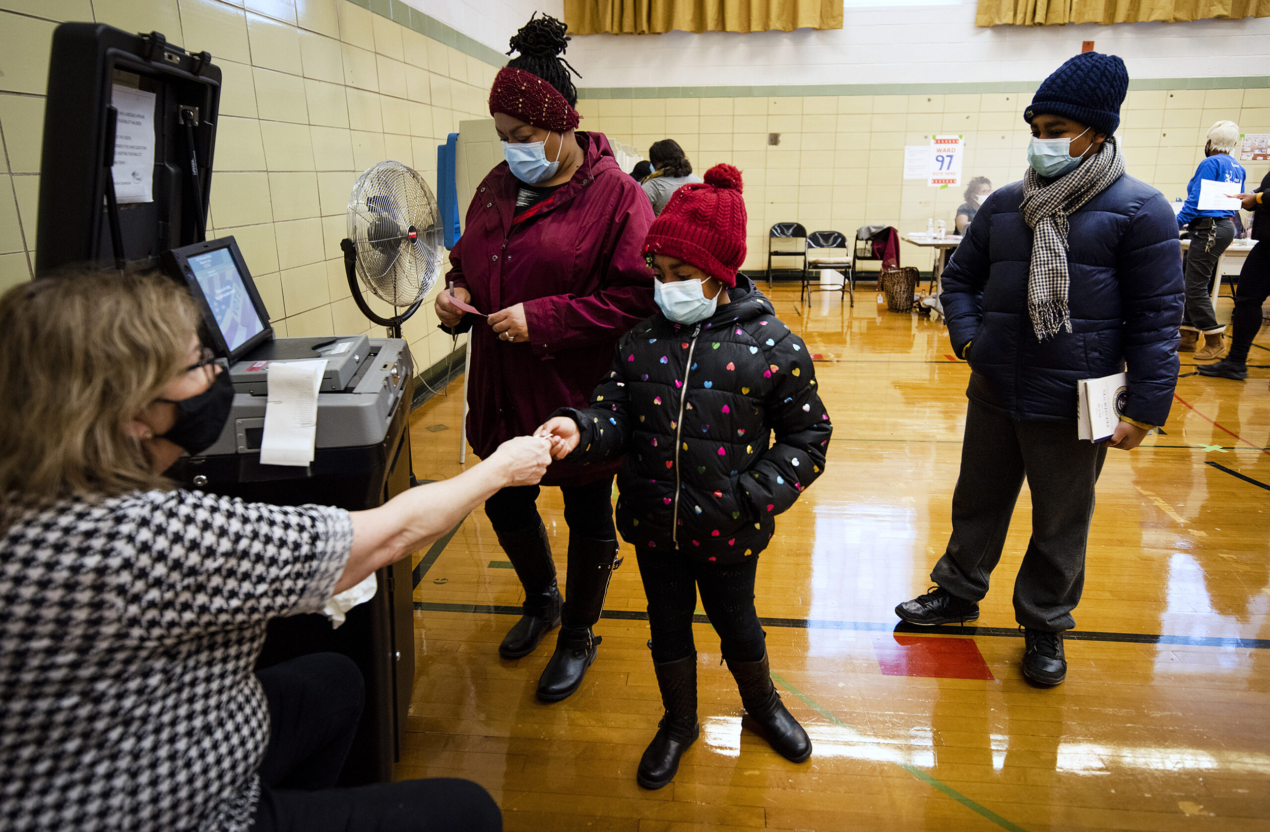 a child reaches out to grab a sticker while standing by the ballot scanning machine