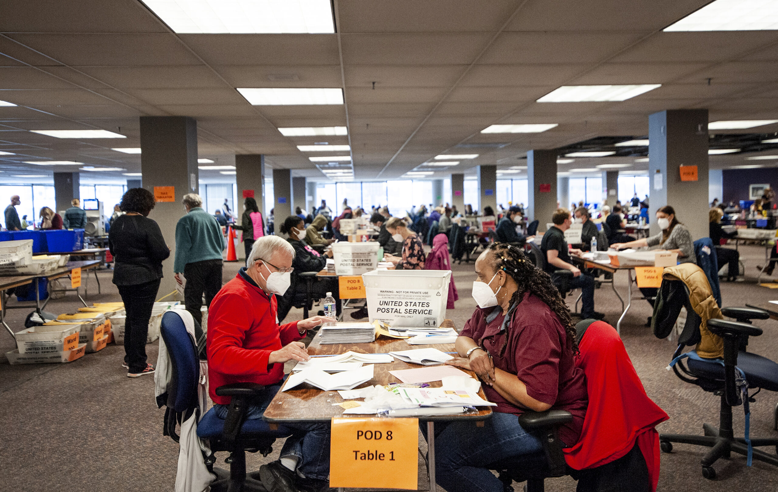 workers at tables sort through ballots in a large room filled with other workers