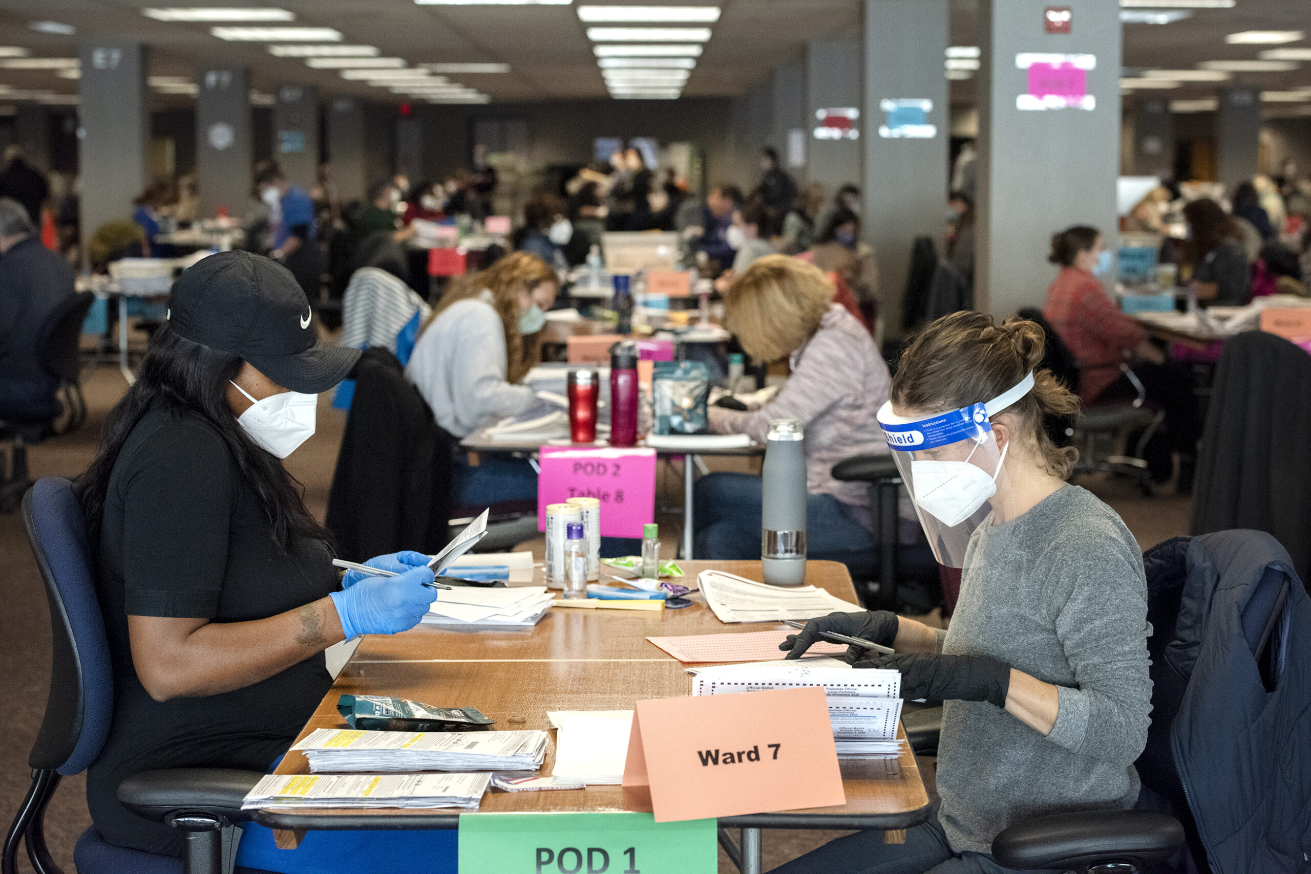 two workers in PPE hold absentee ballots as they sort them at a table