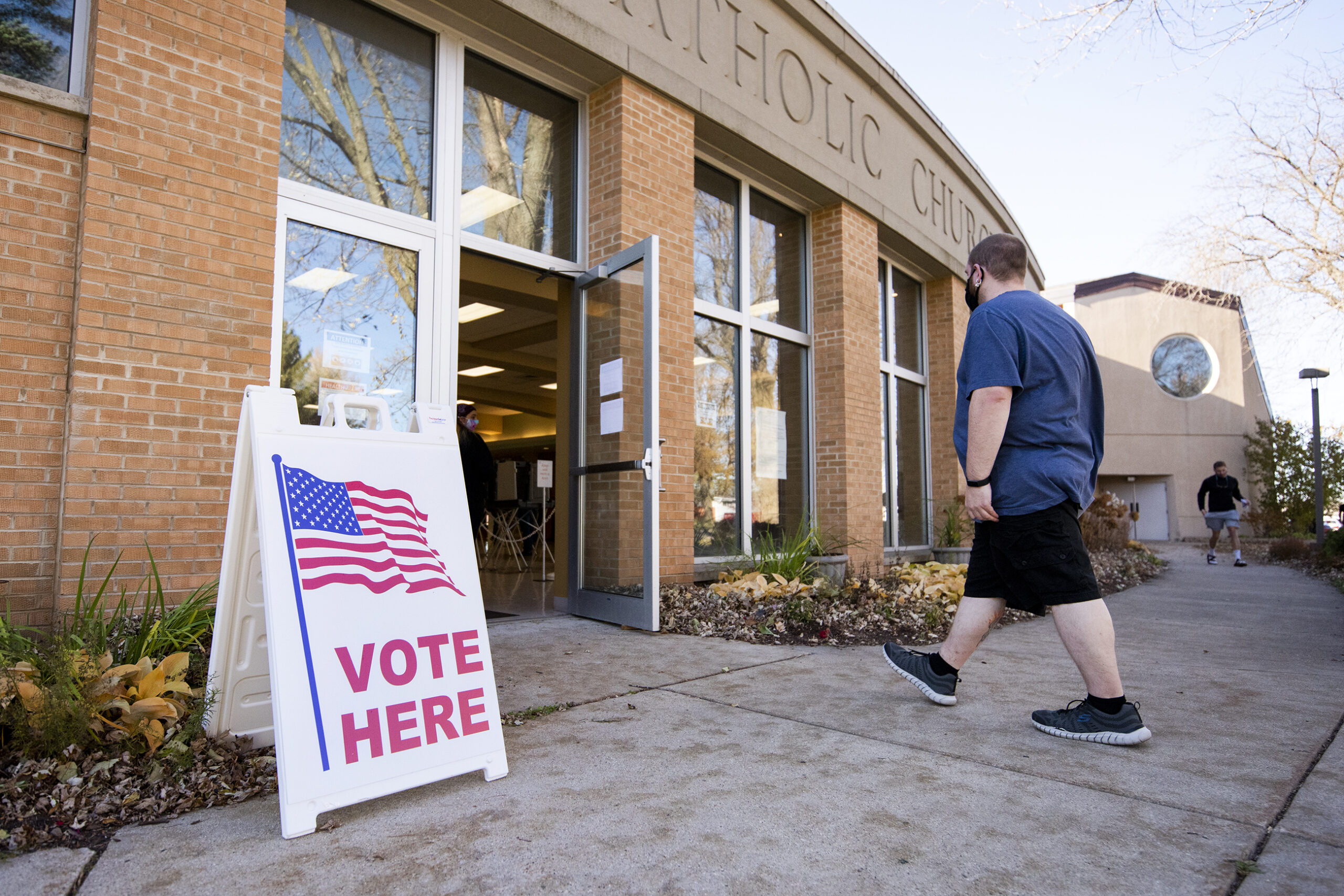 a voter walks into a polling location. a sign says "vote here."