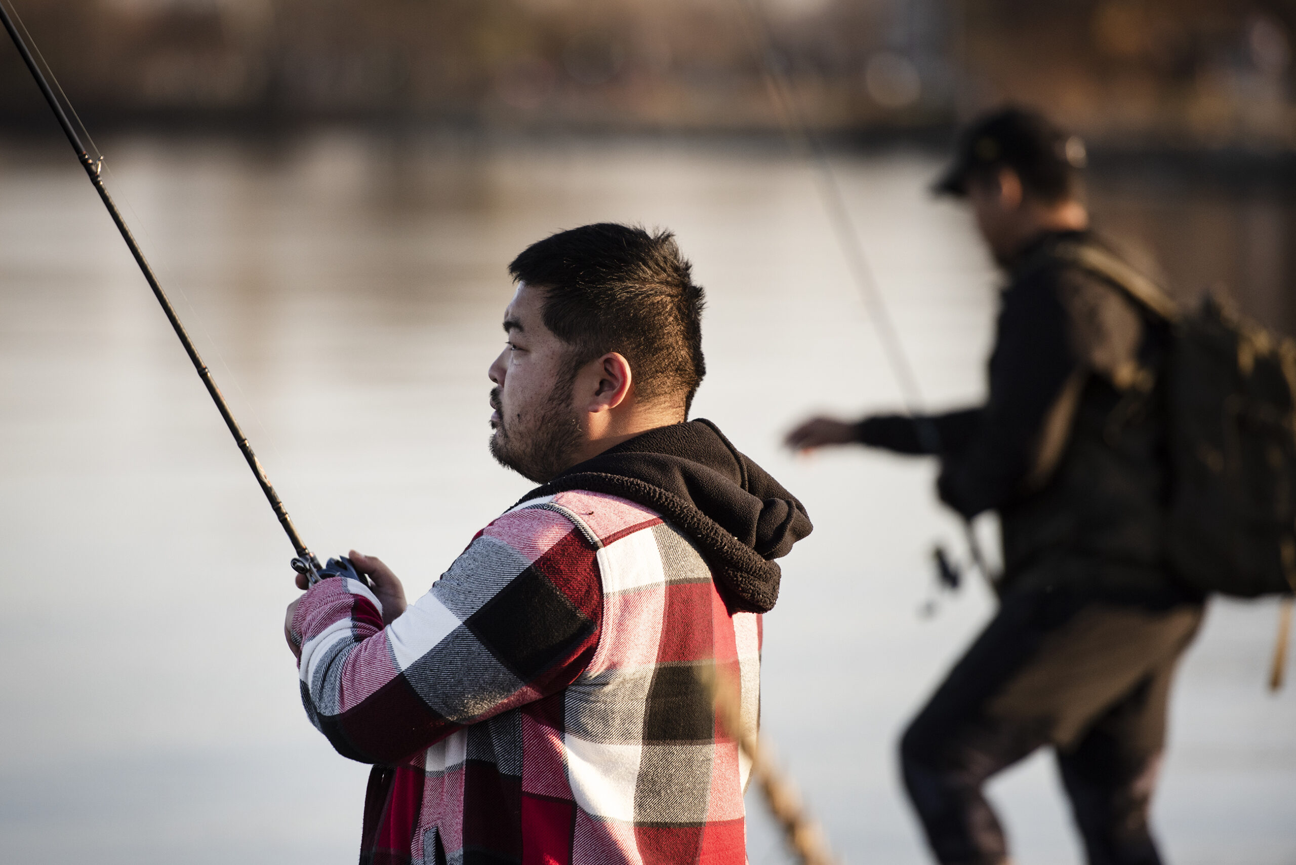 two men hold their fishing rods as afternoon light bounces off Lake Monona