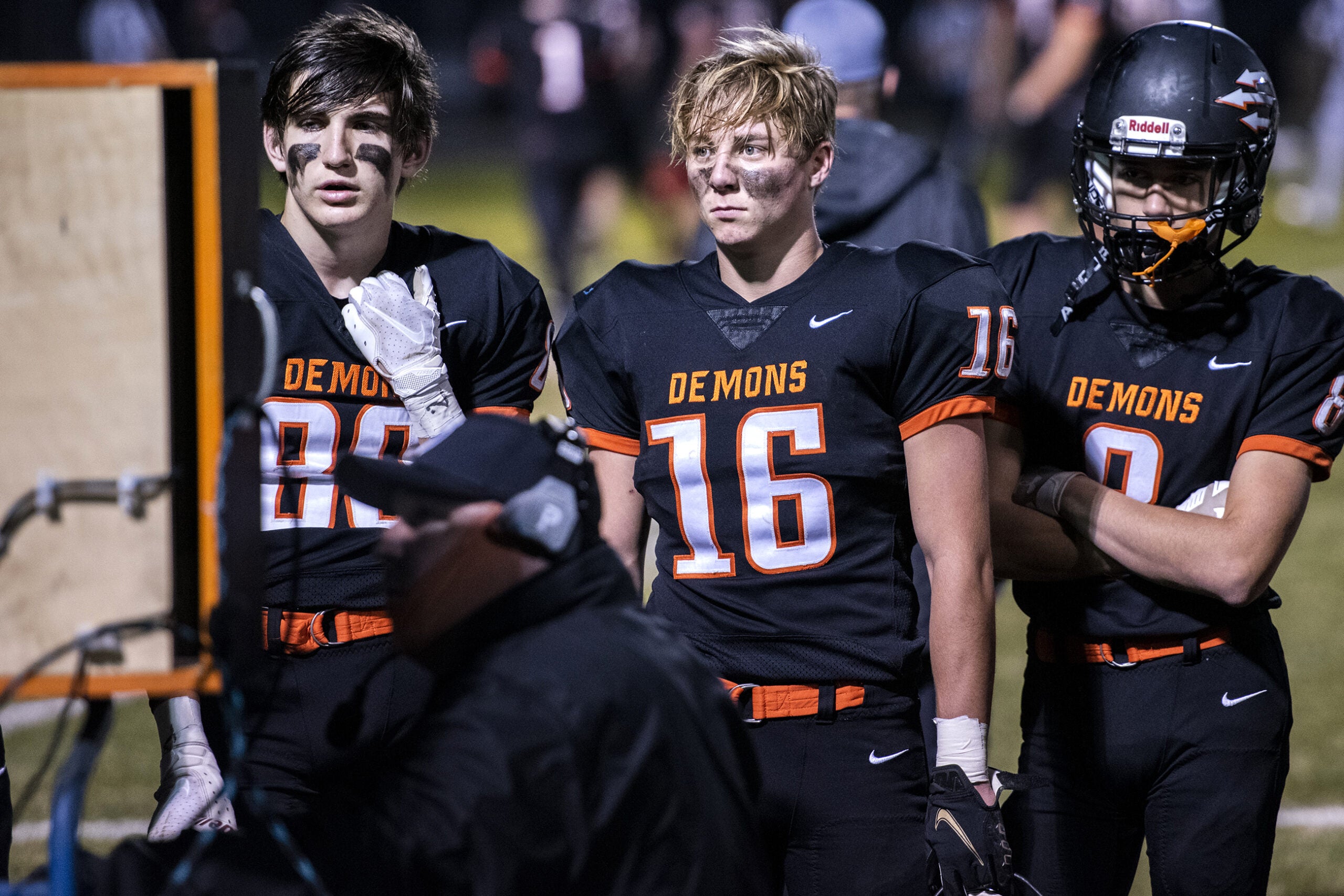 three football players gather around a screen as a coach speaks to them