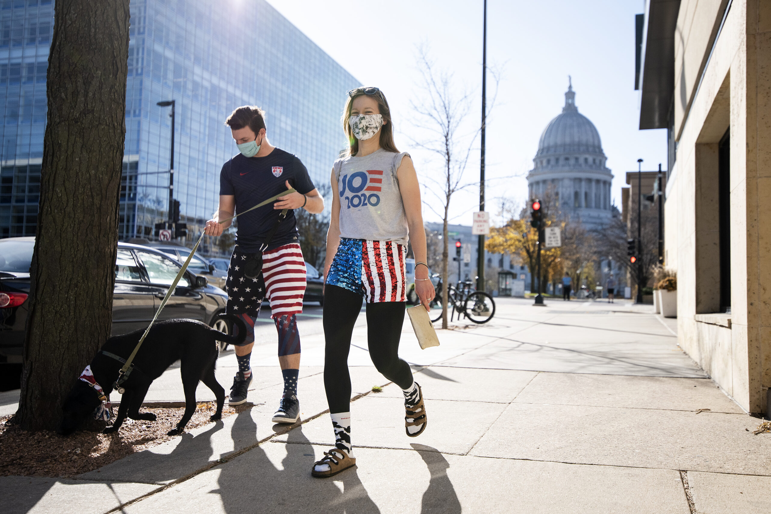 two people in U.S. flag printed shorts walk a dog. a woman wears a 