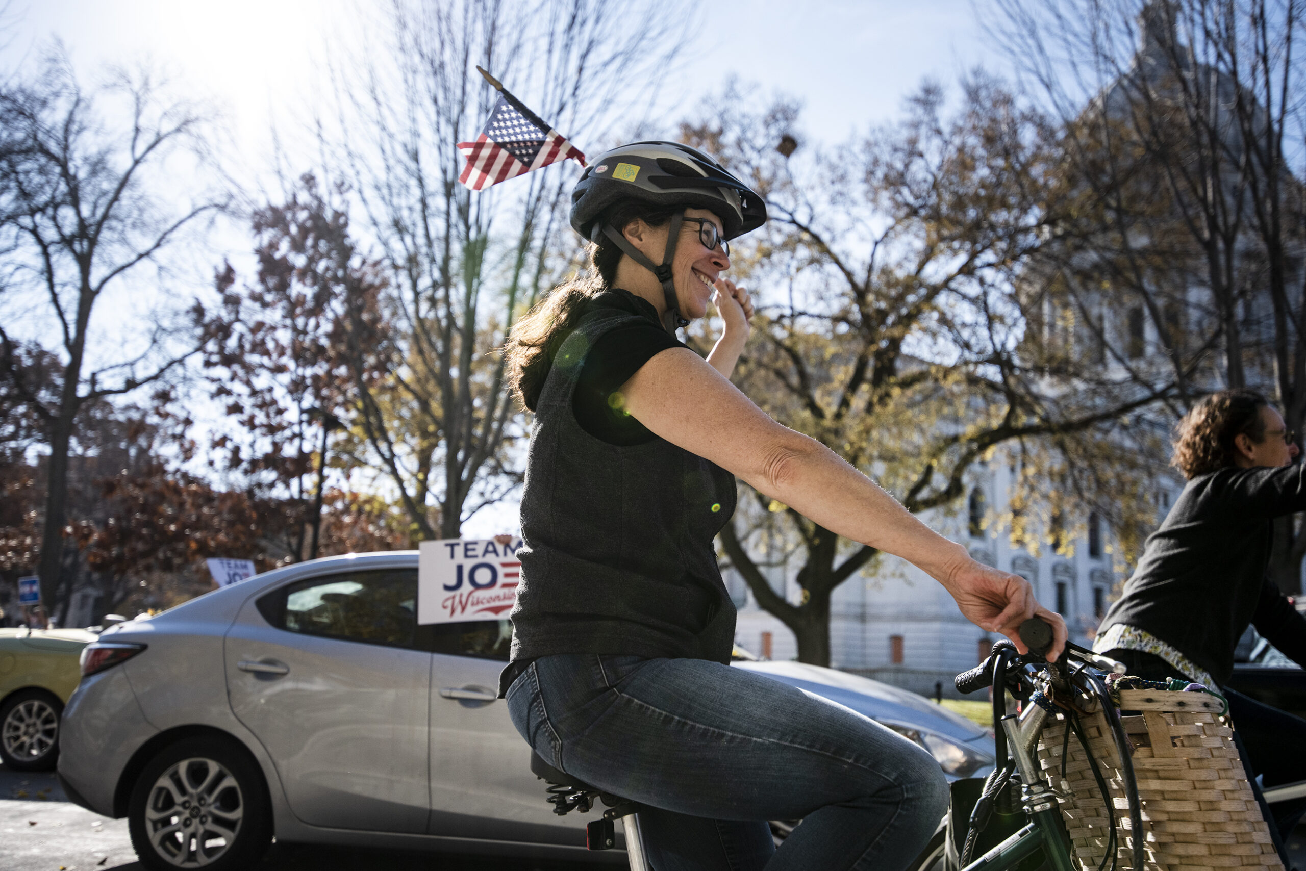 a woman on a bike smiles as she waves a U.S. flag