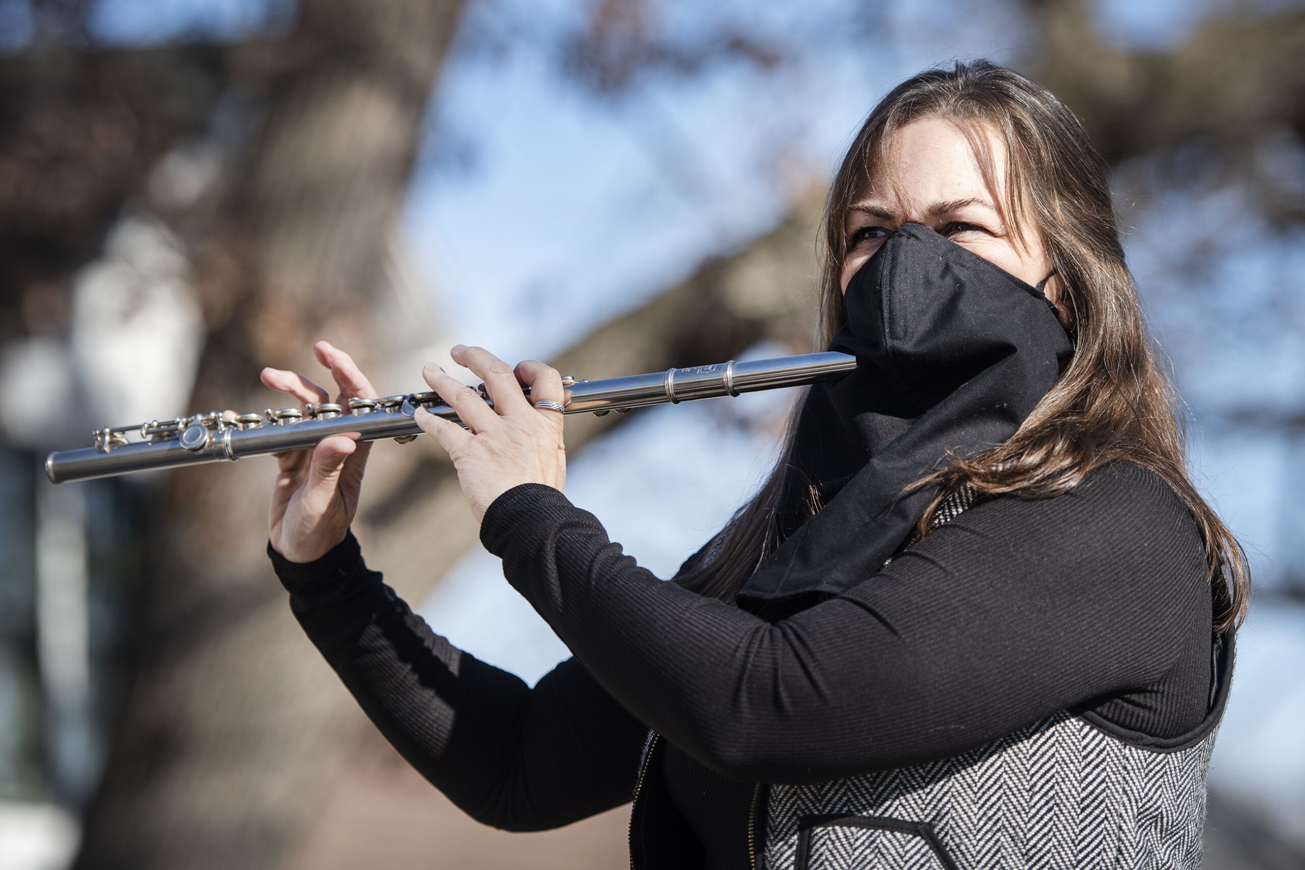 A woman plays a flute through a hole in a black face mask