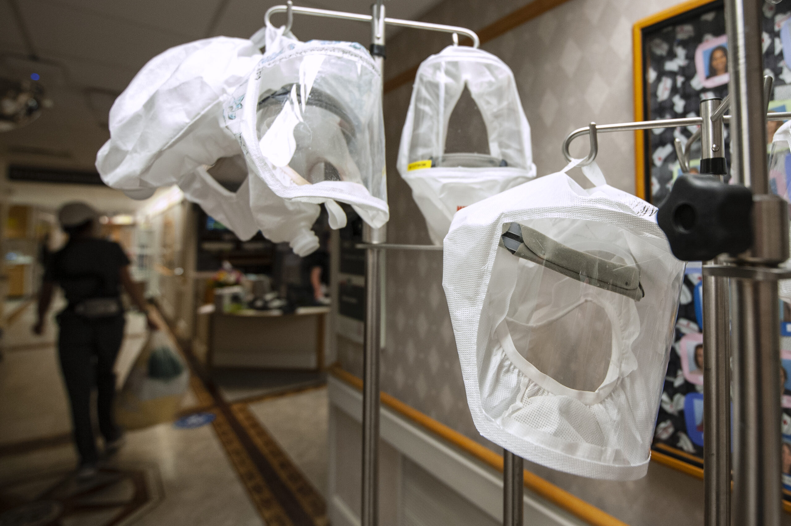 Large protective hoods hang on a rack in a hospital hallway