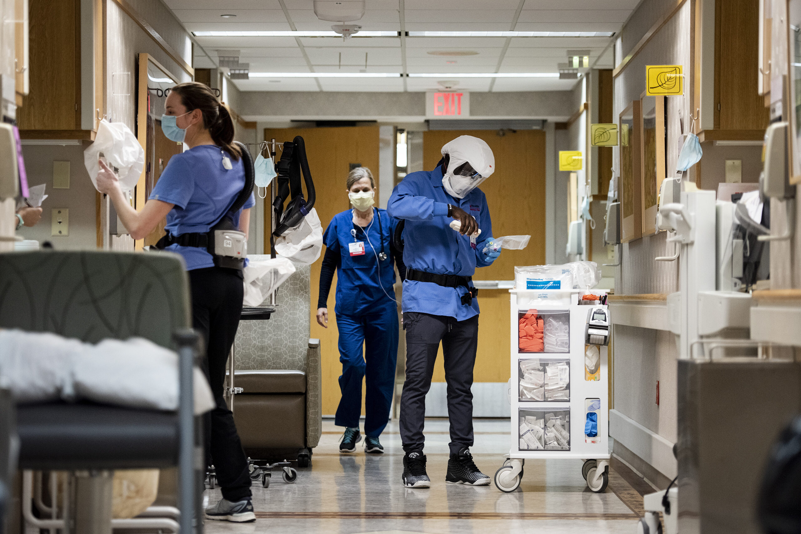 Several healthcare workers perform different tasks in a hospital hallway