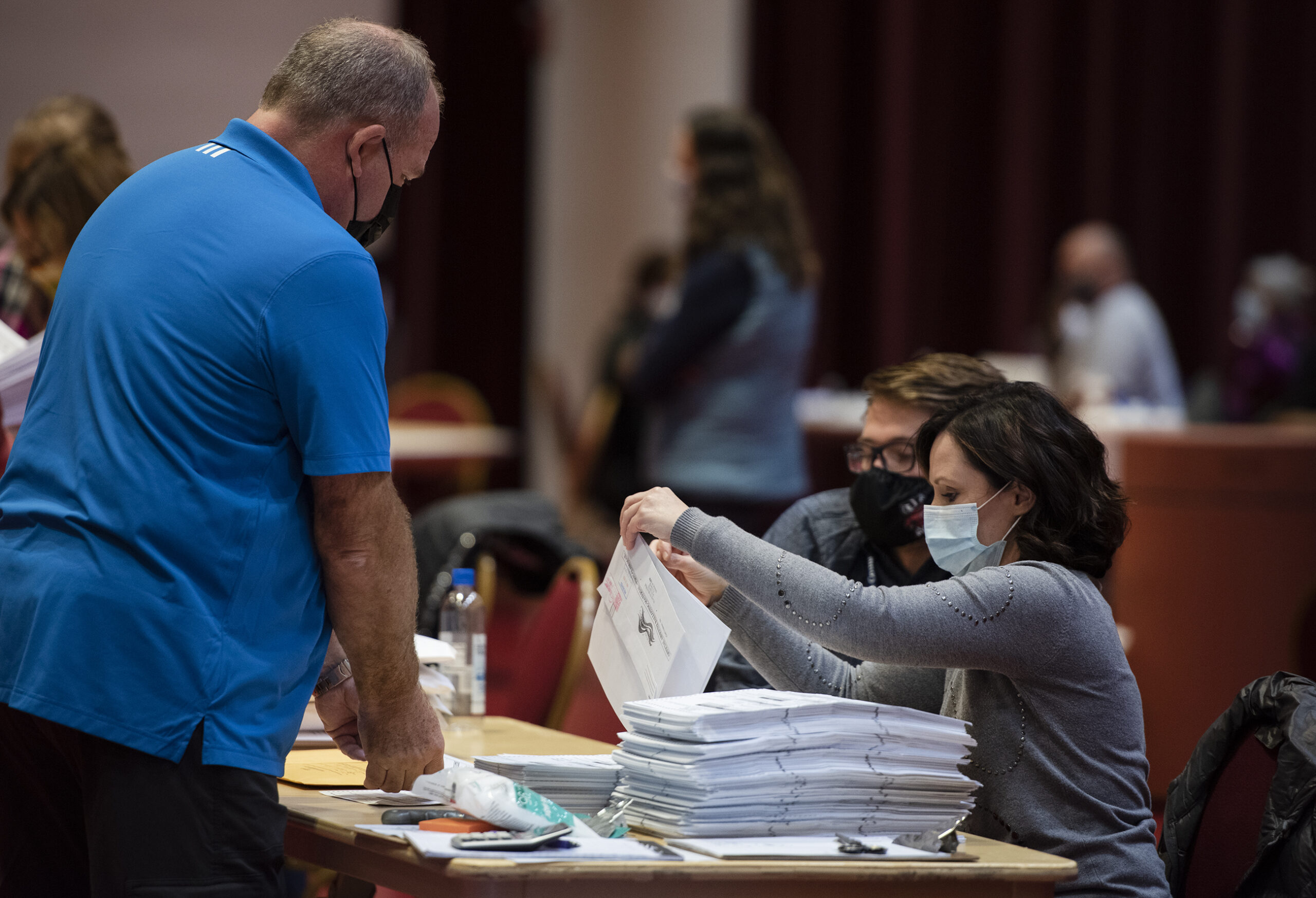 Two workers go through a large stack of ballots on a table