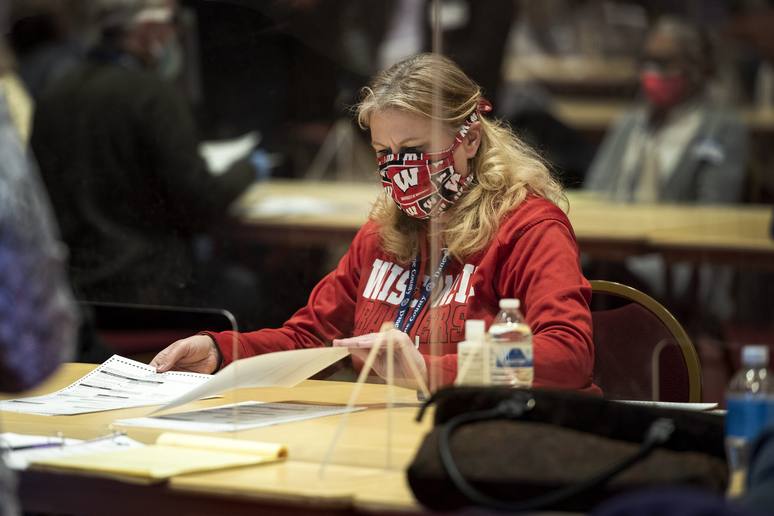 A woman sits behind plexiglass and flips through ballots