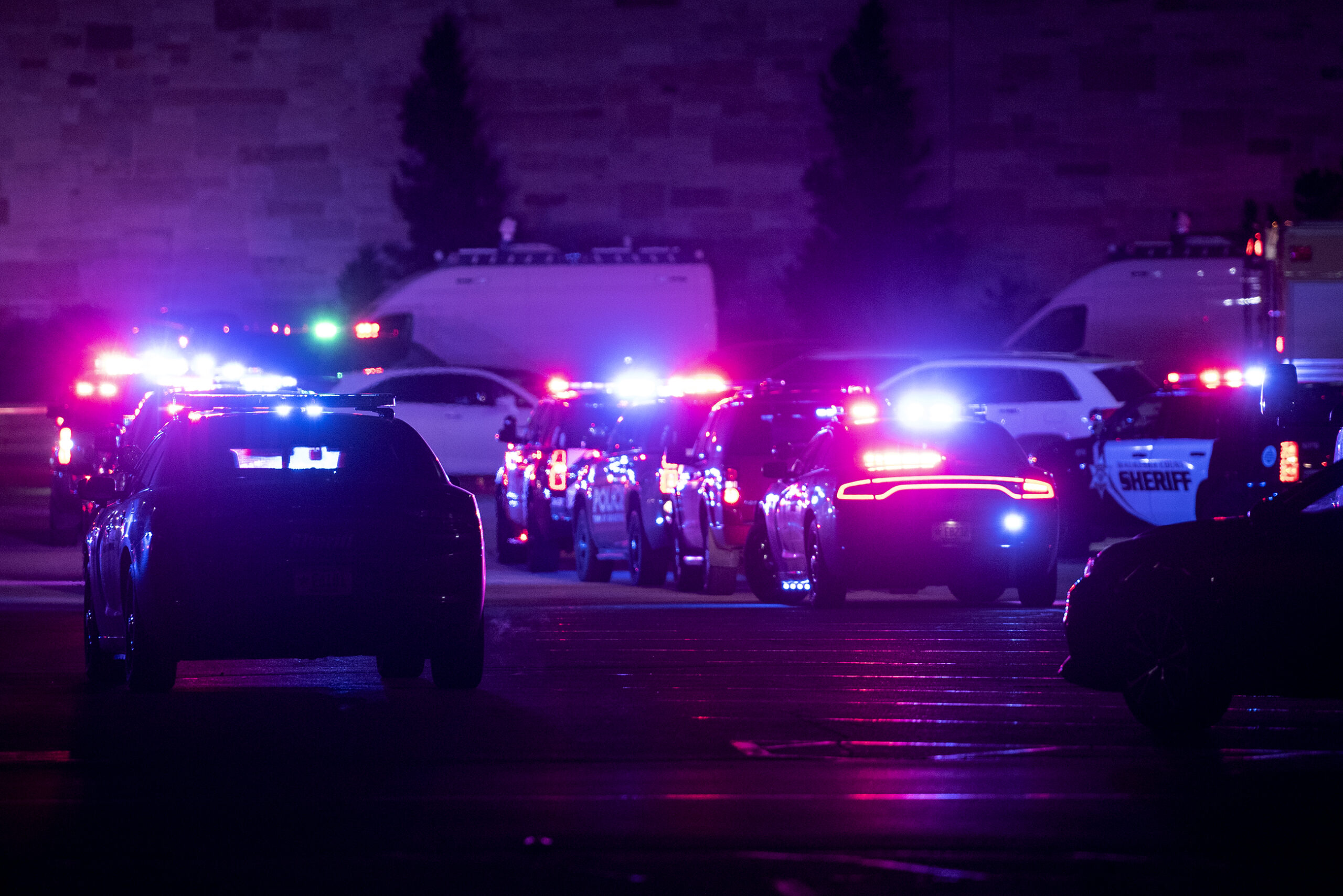 Red and blue lights from police cars illuminate a dark parking lot