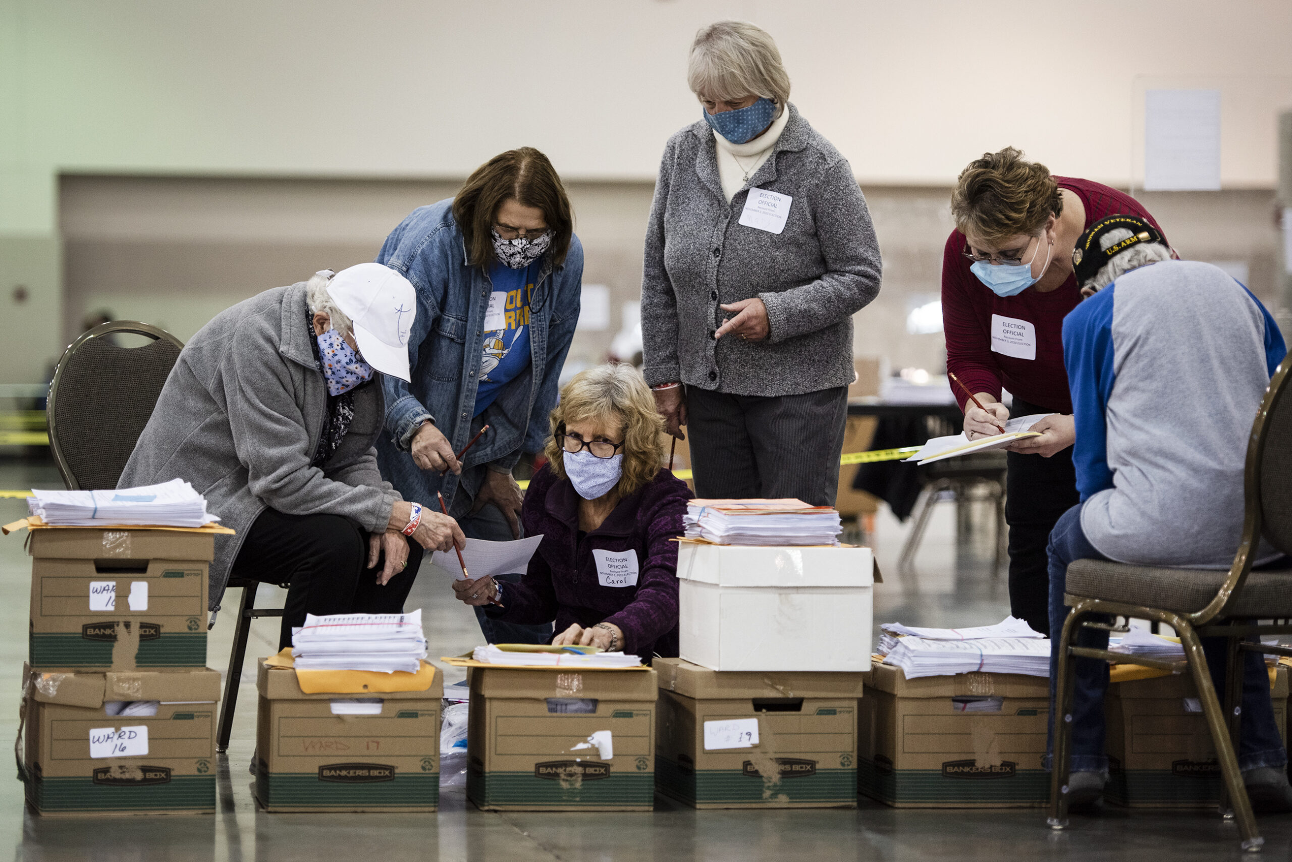 Six people gather around boxes on the floor as they look through documents