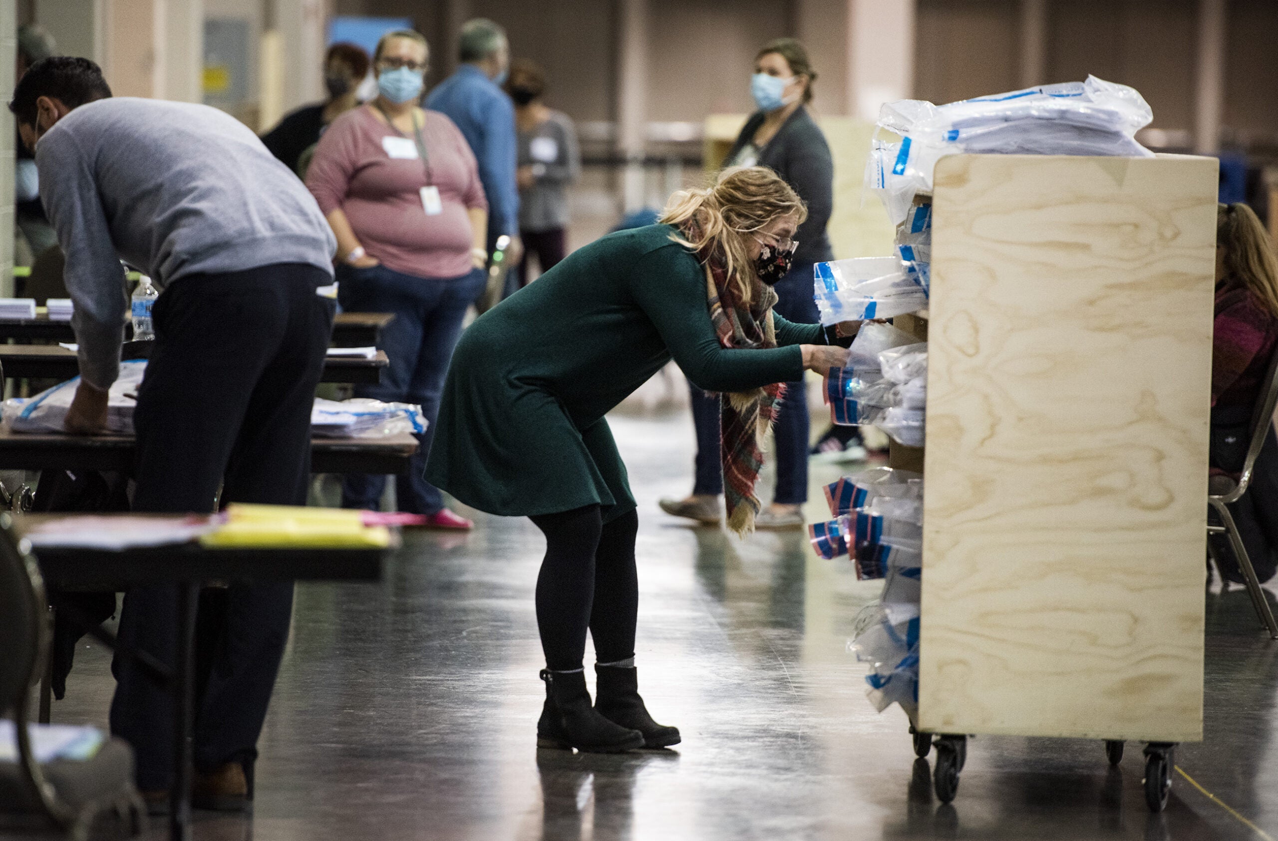 A woman reaches into a wooden cart to grab a bag containing ballots