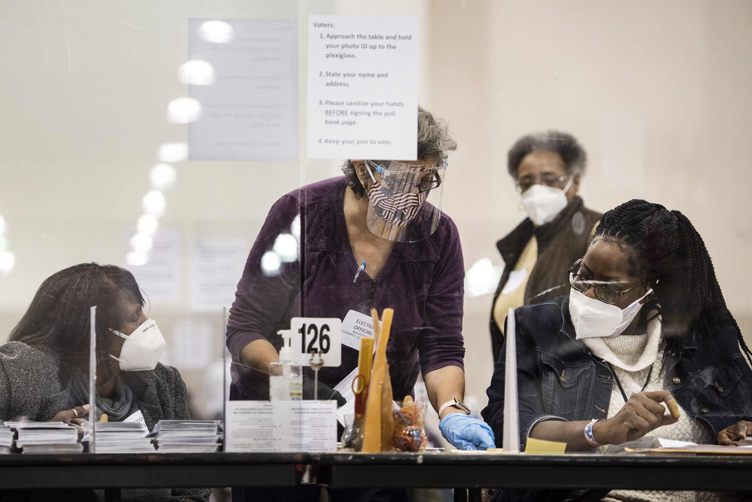 A woman in a US flag face mask and face shield speaks to two other election observers
