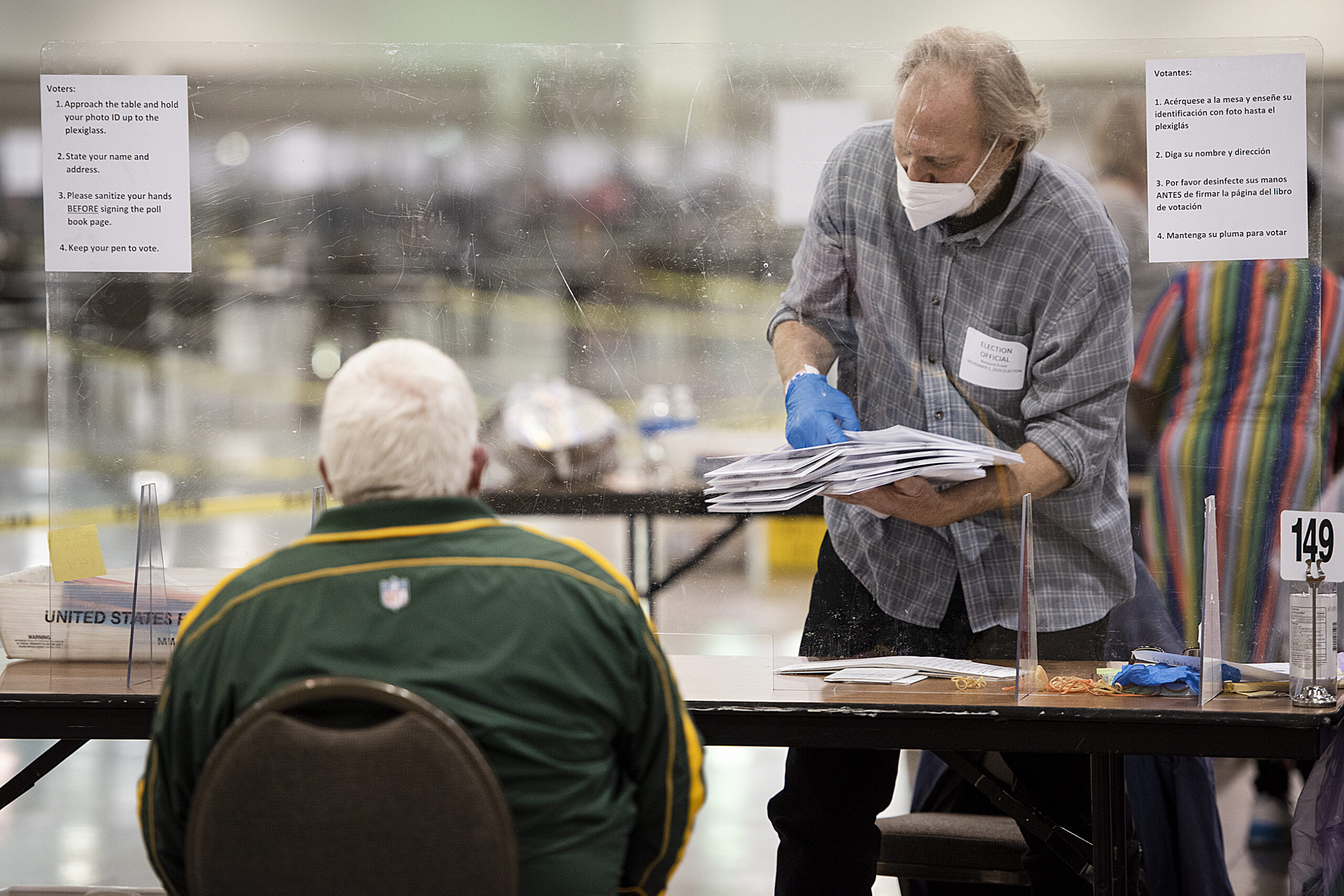 A man in gloves and a face mask carries a stack of ballots during the recount