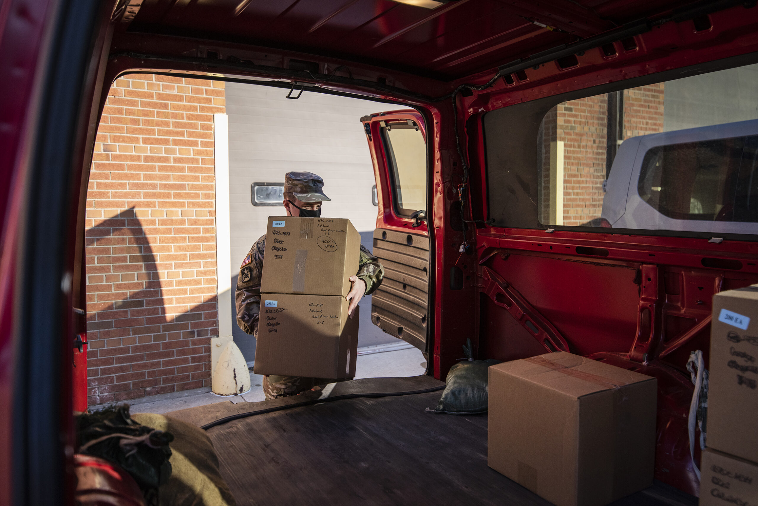 A man in a military uniform carries two boxes into the back of a van