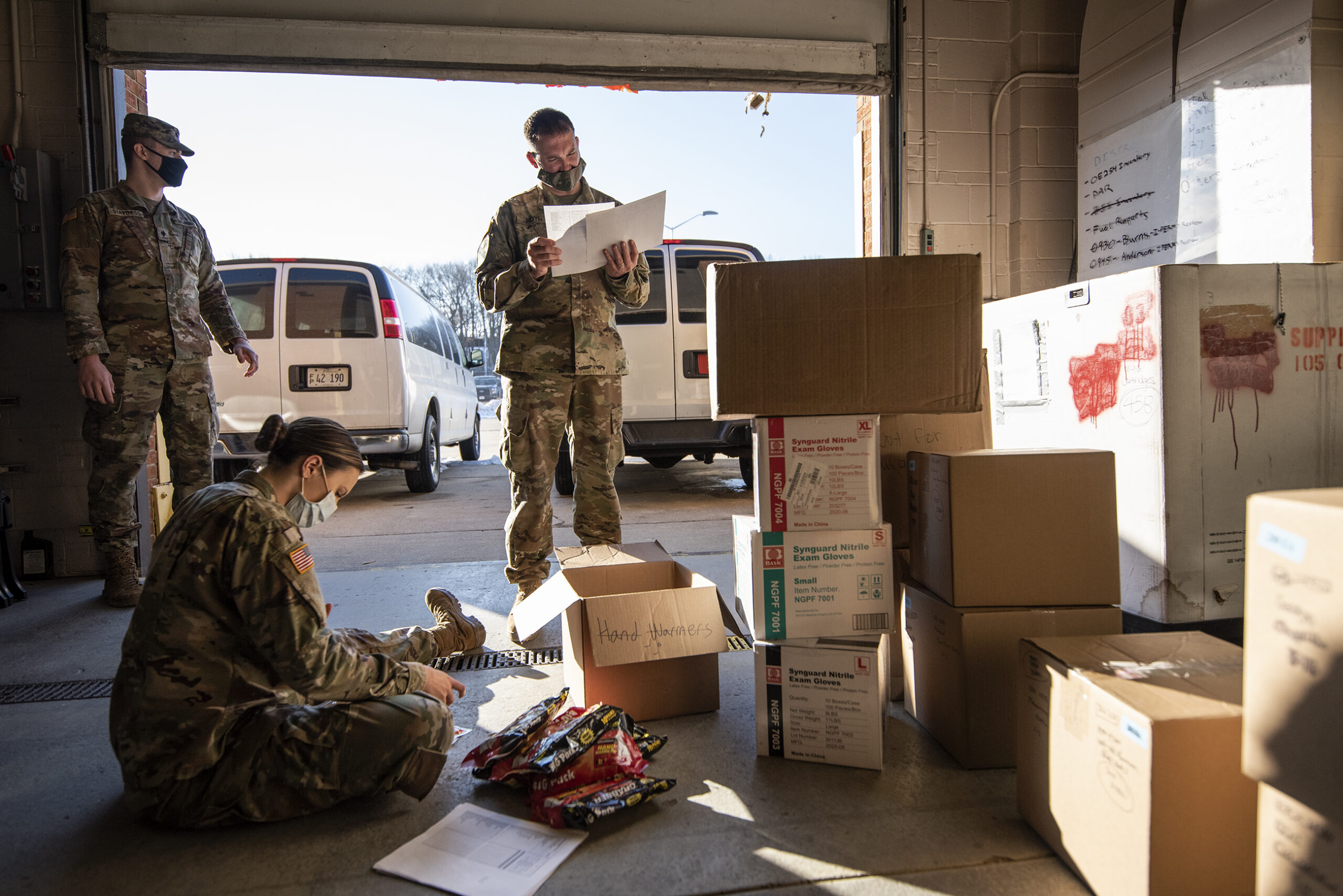 three Wisconsin National Guard members gather around cardboard boxes before loading them into vans