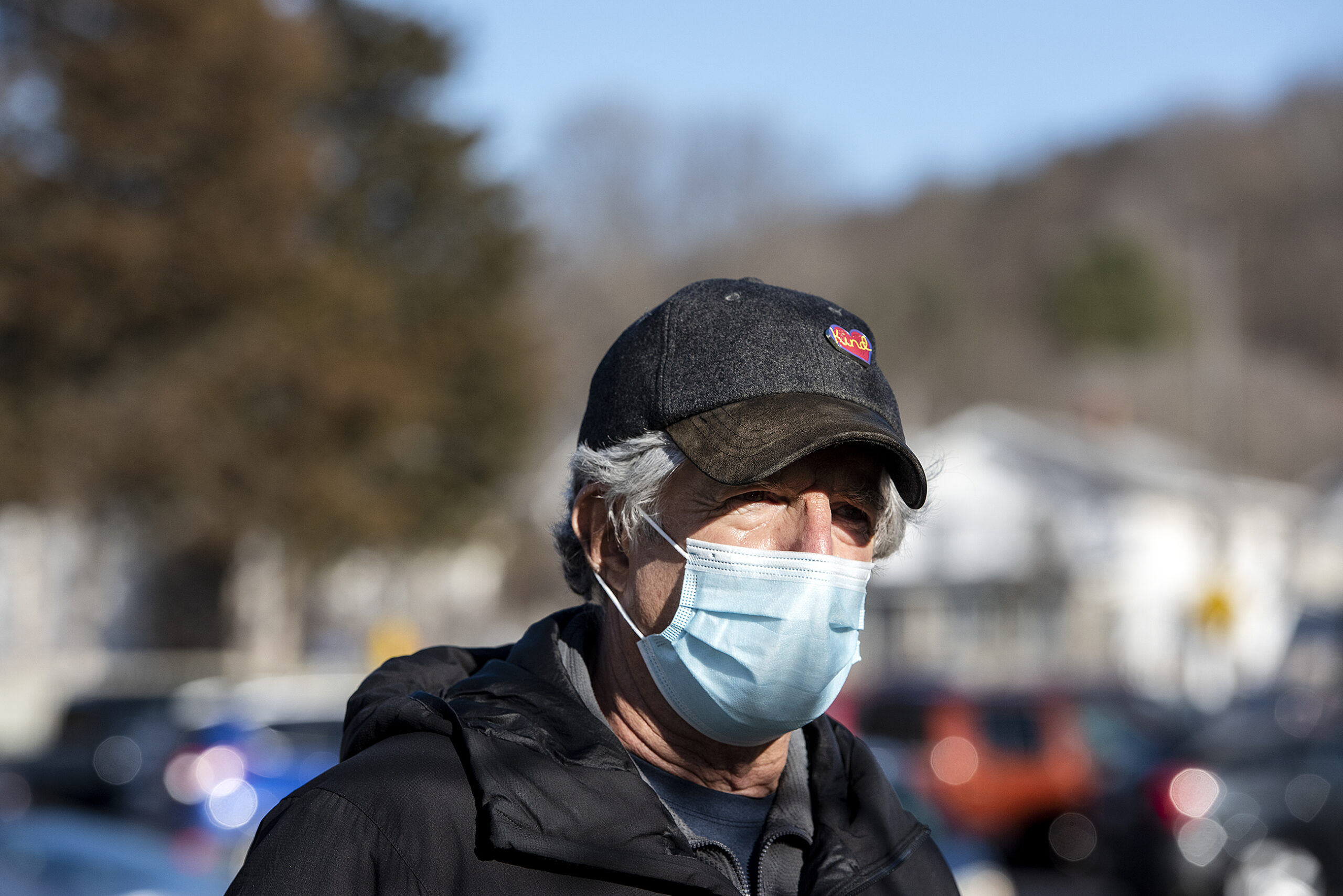 A man in a cap and face mask stands outside