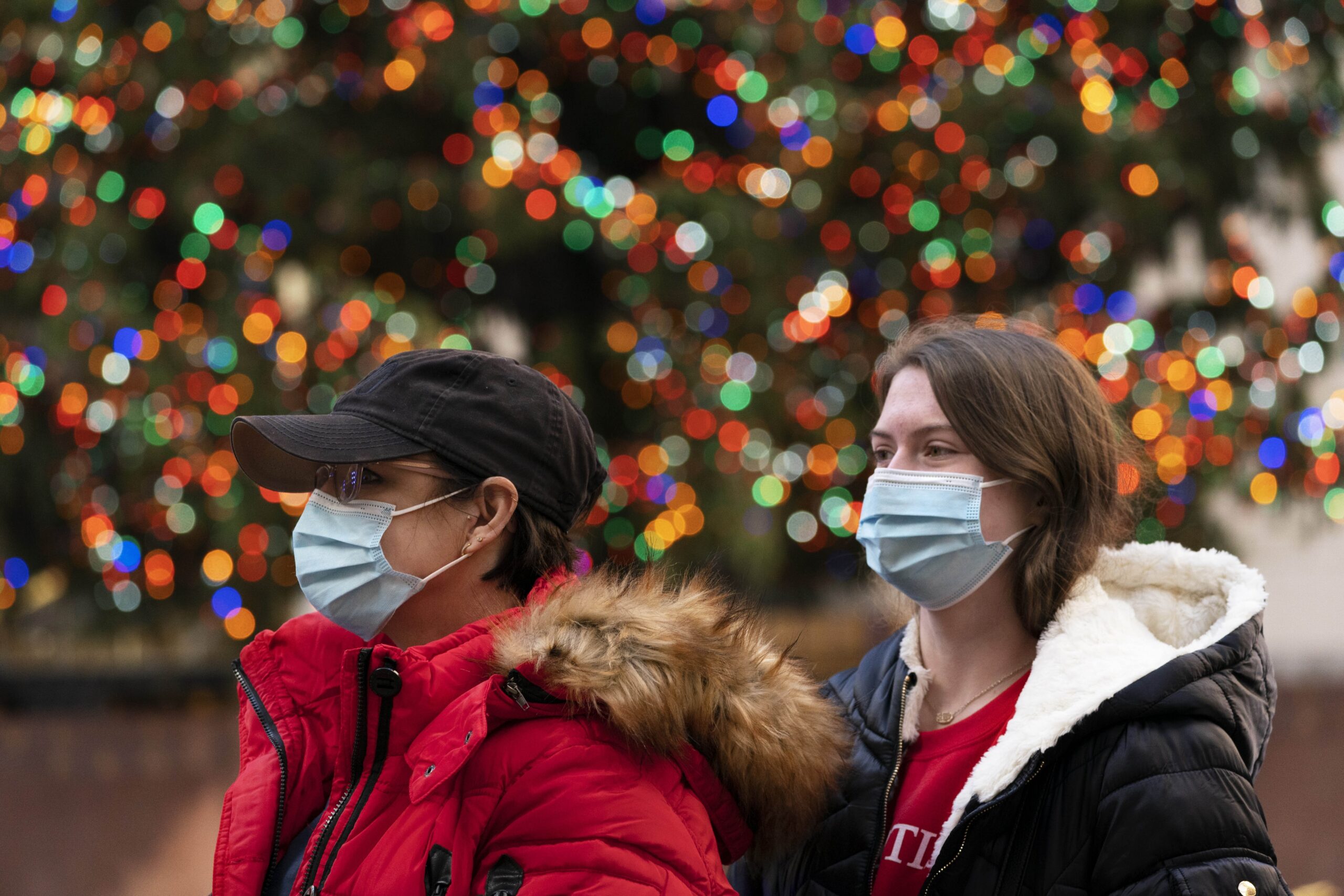 People walk by the Rockefeller Center Christmas Tree wearing face coverings