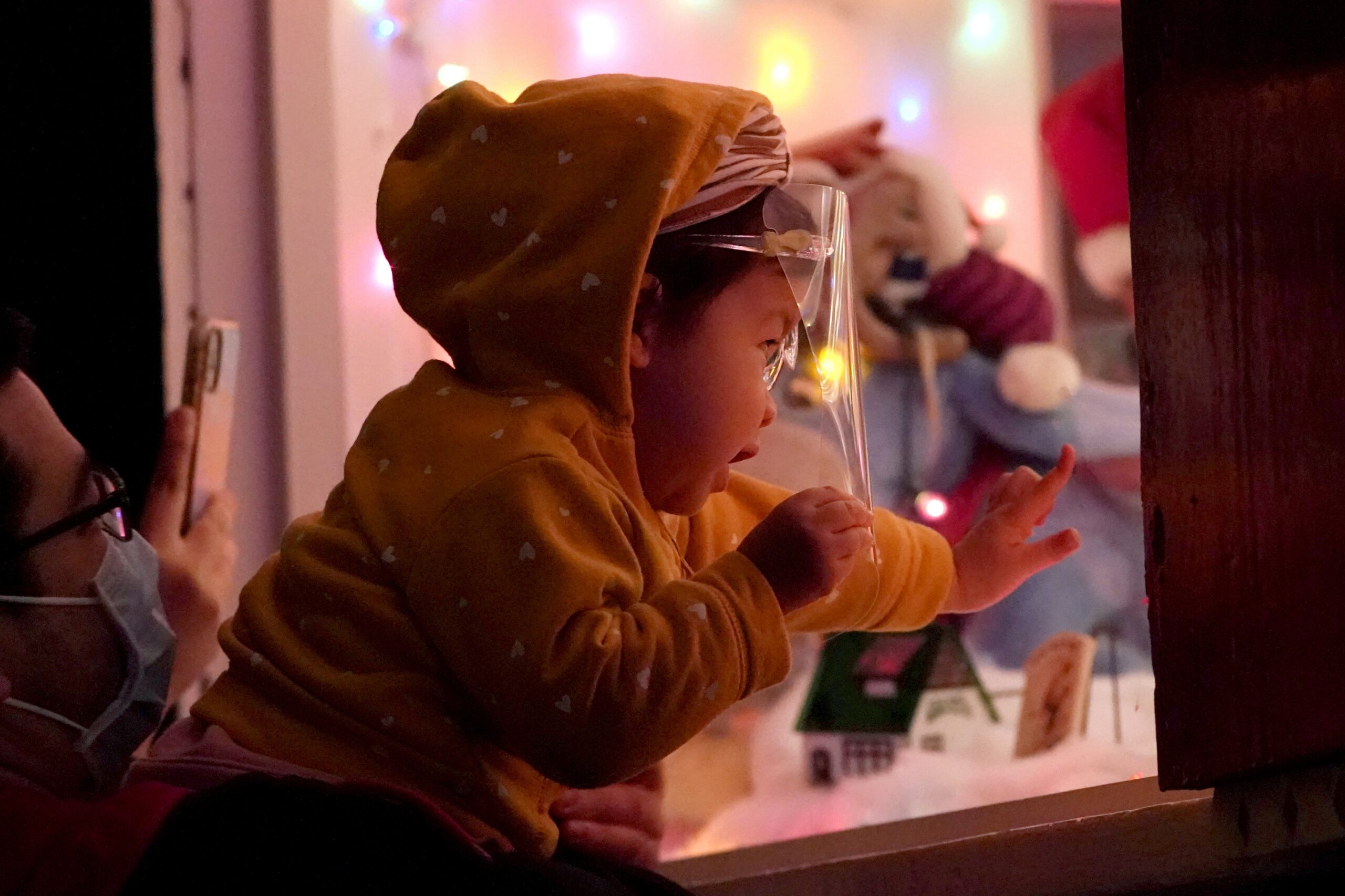 Meya McPalmer, 1, wears a face shield to protect against COVID-19 while peeking into the Christmas display