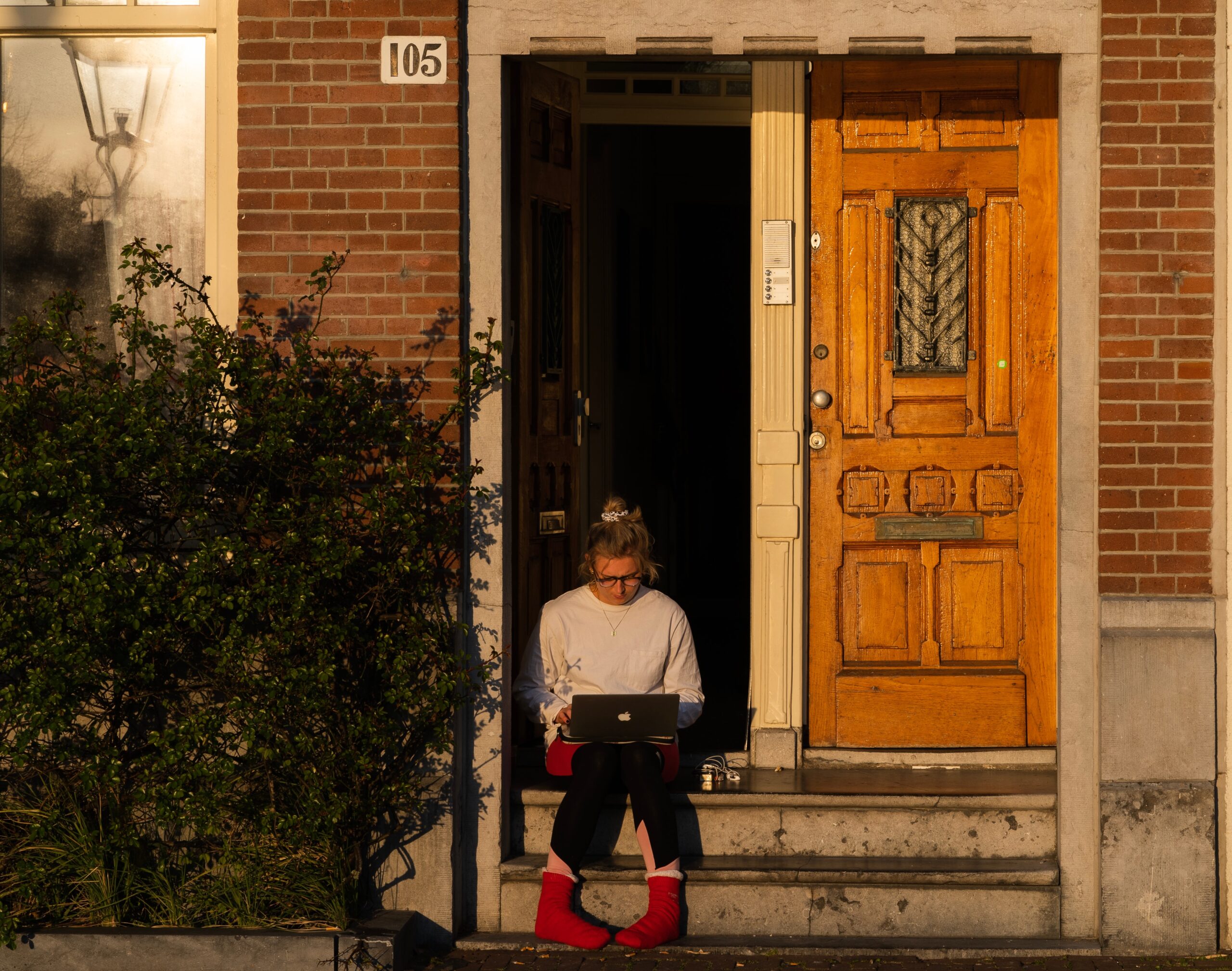 A woman sits on a stoop while using her computer.