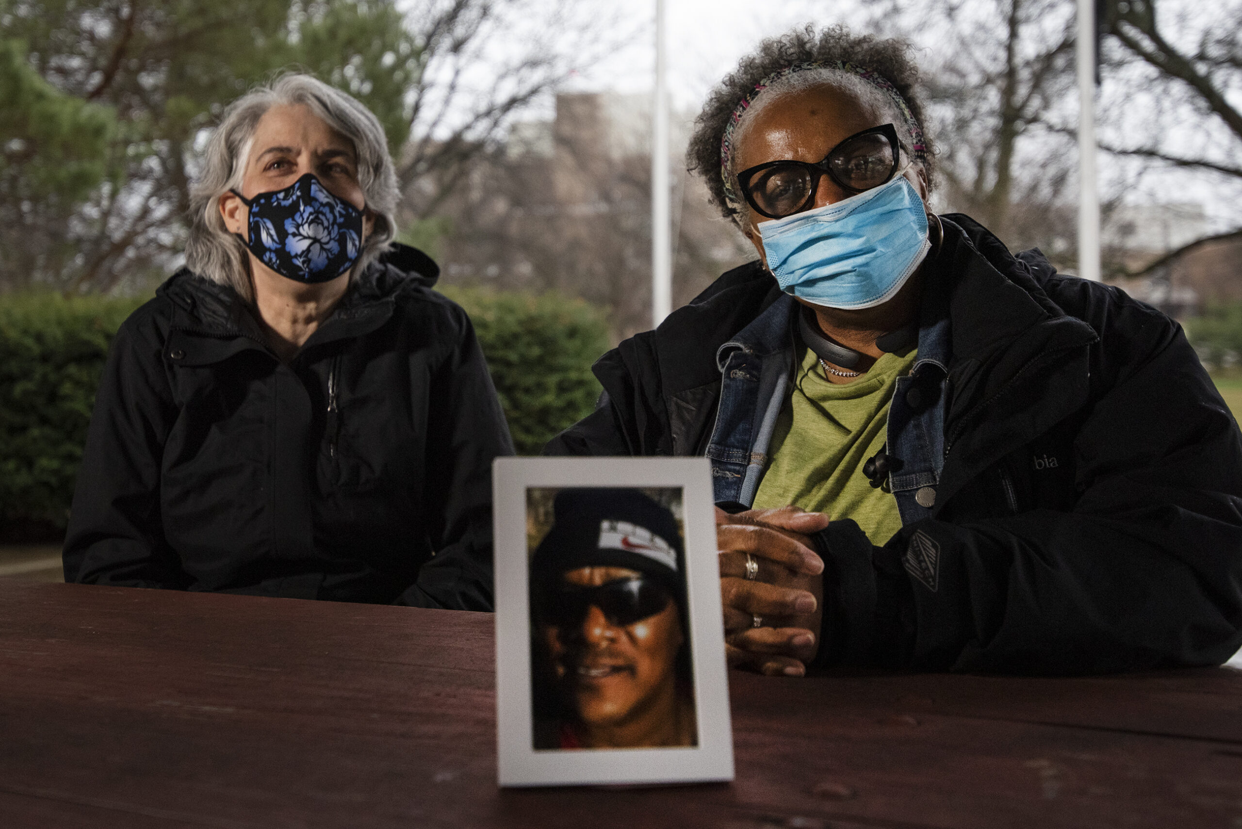 two women sit at a table in face masks with a photo of Charles