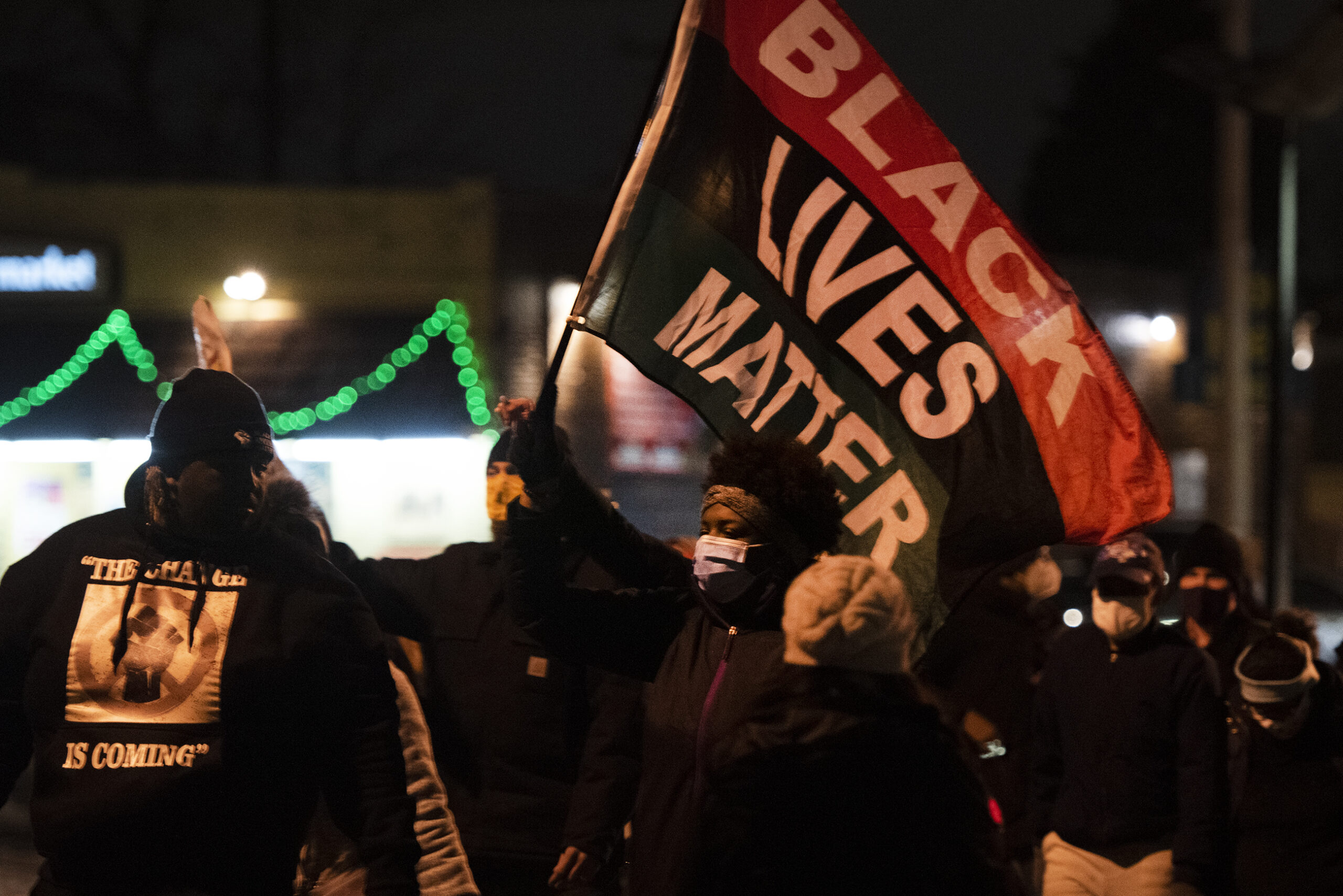 a black lives matter flag is held up by a protester in a face mask