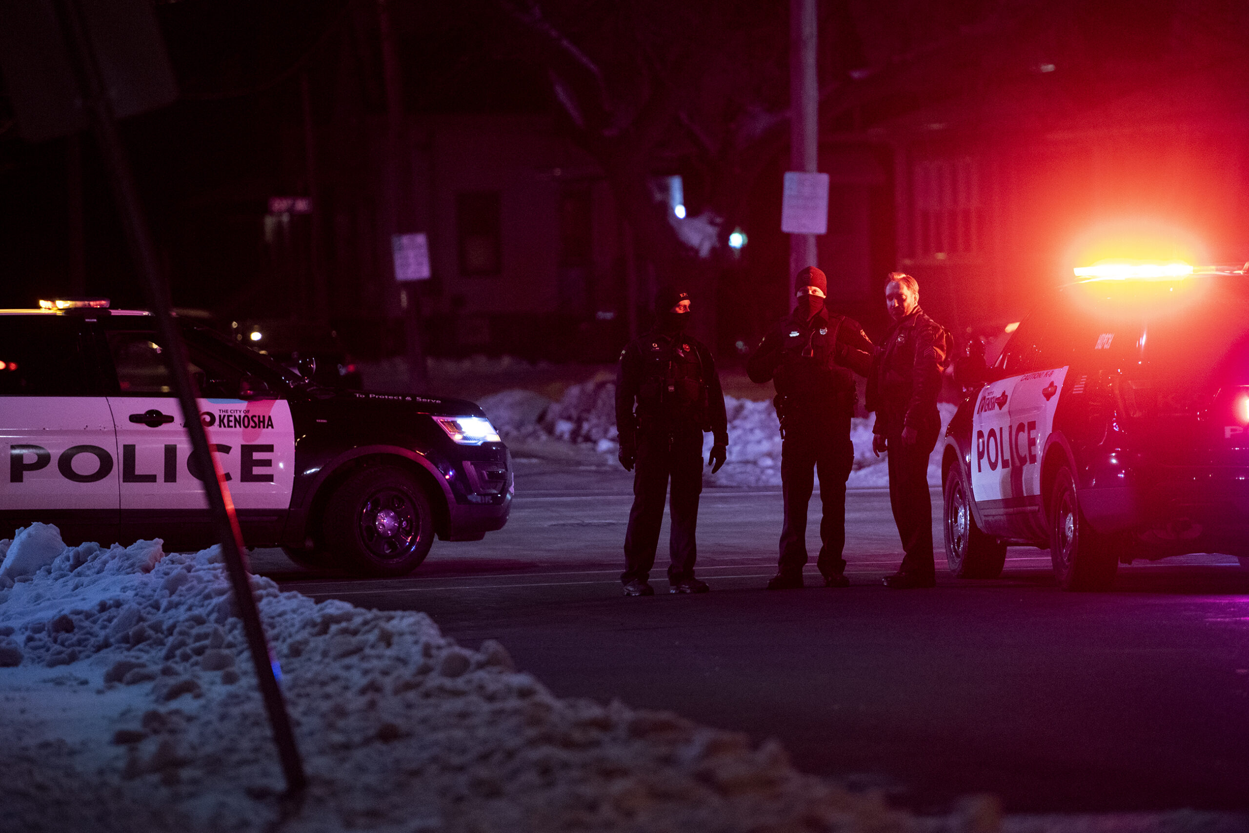 red police lights fill the darkness as three police officers stand together in a road