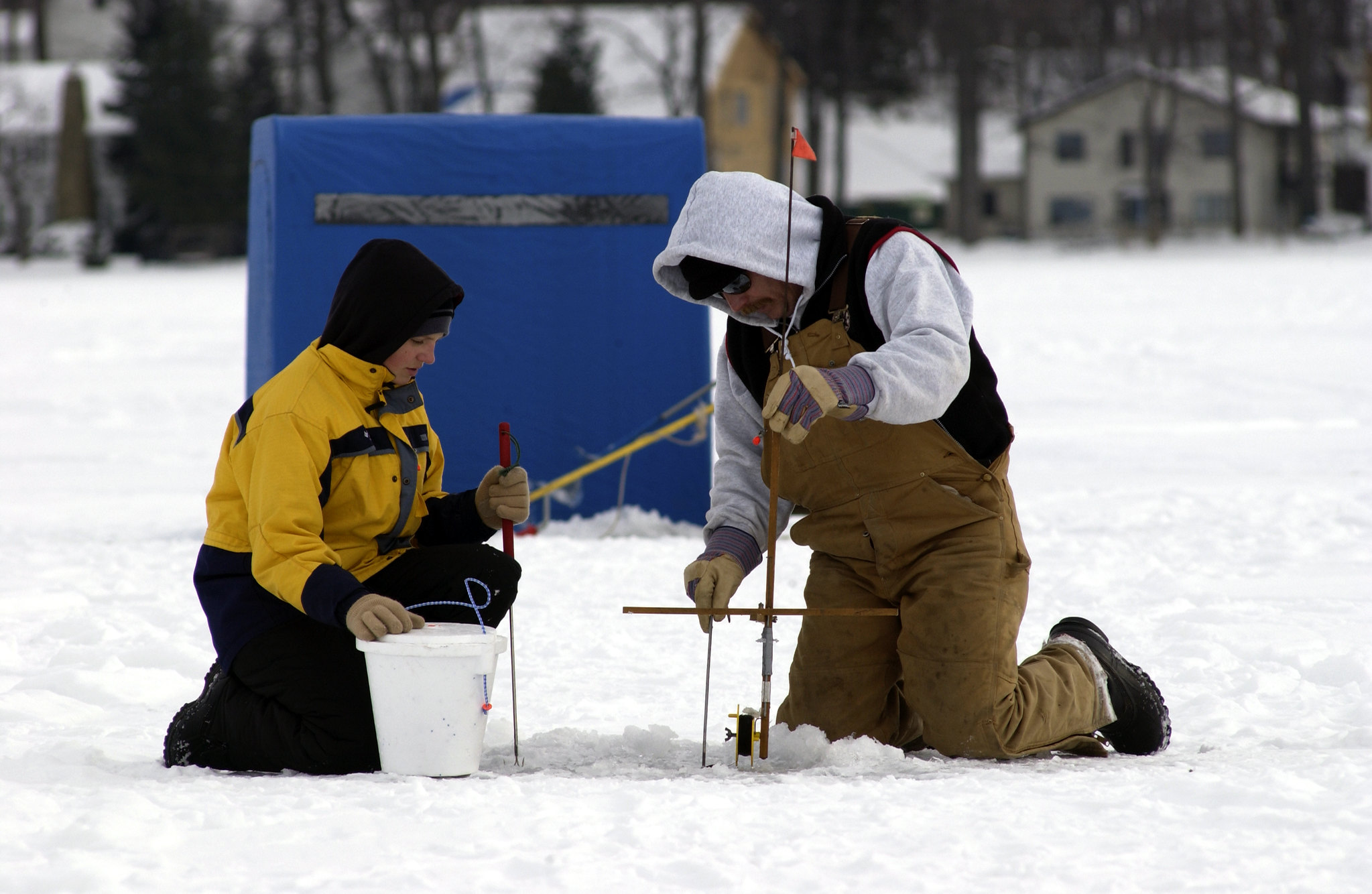 Two people ice fishing on frozen lake.