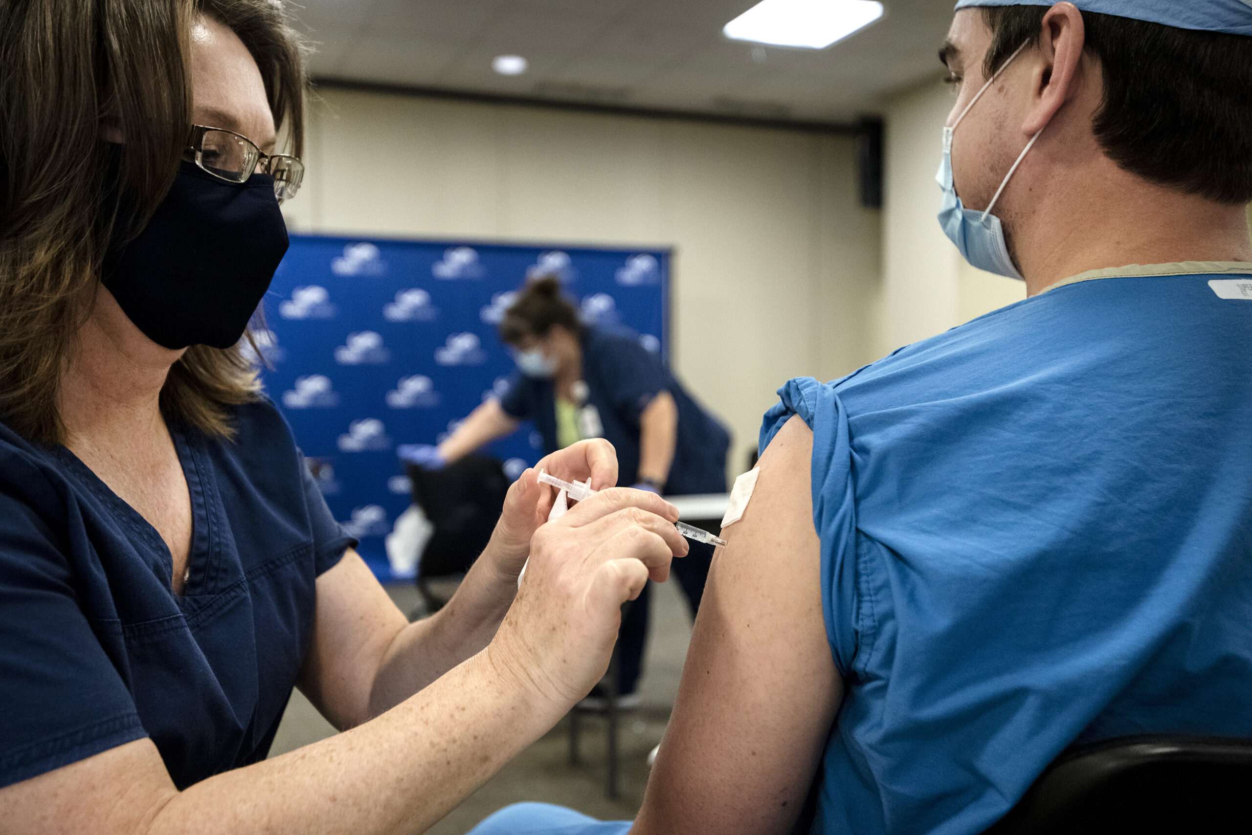 A nurse in a face mask gives a vaccine to a fellow healthcare worker in scrubs