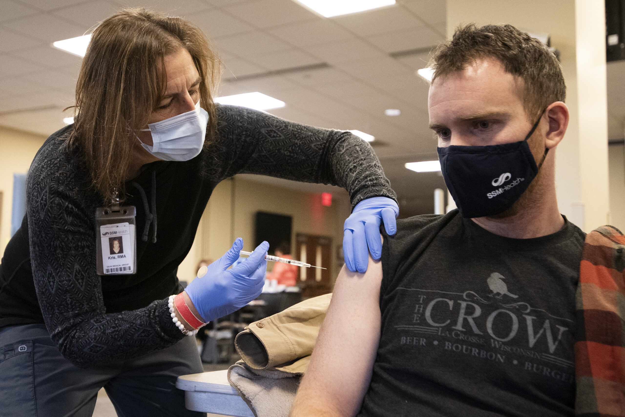 A nurse wears blue gloves as she gives a vaccine to a man with rolled up sleeves
