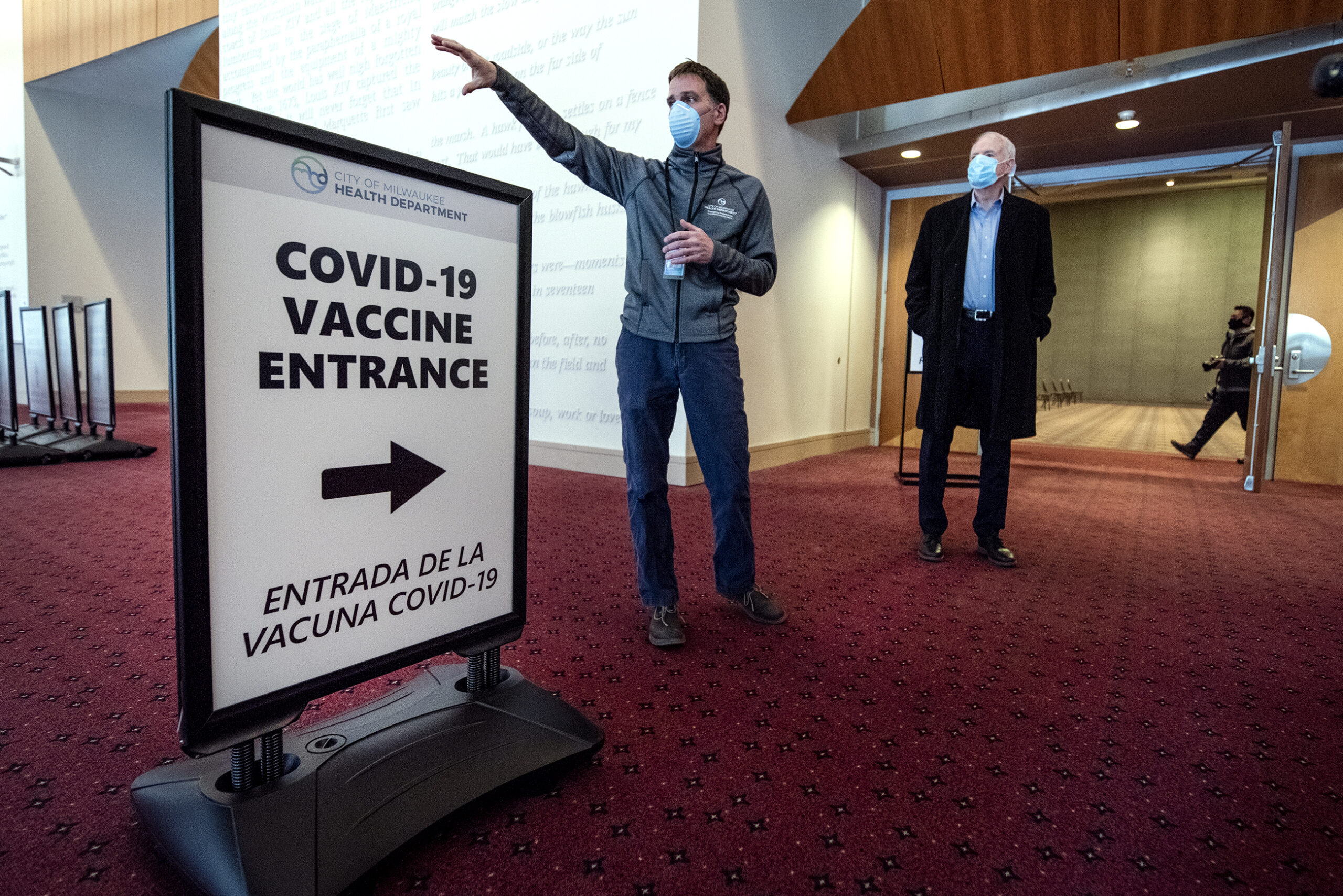 Two men in face masks stand by a sign that says 