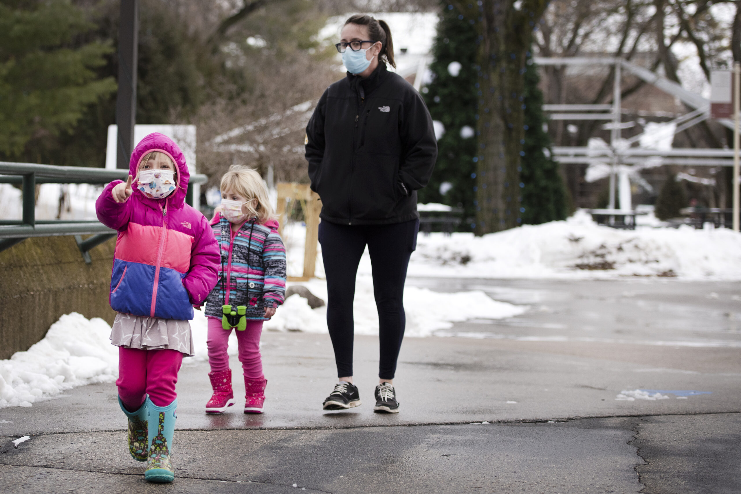 Two children walk with an adult, all in face masks, at the zoo