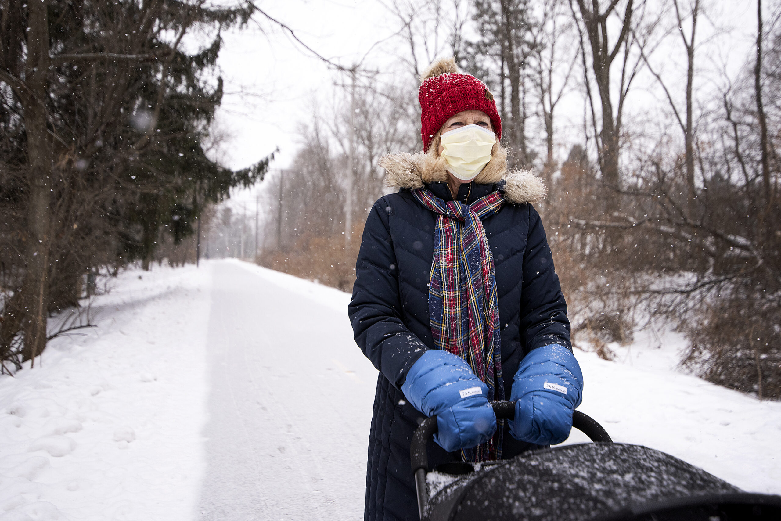 A woman in a face mask and winter gear walks outside in the snow