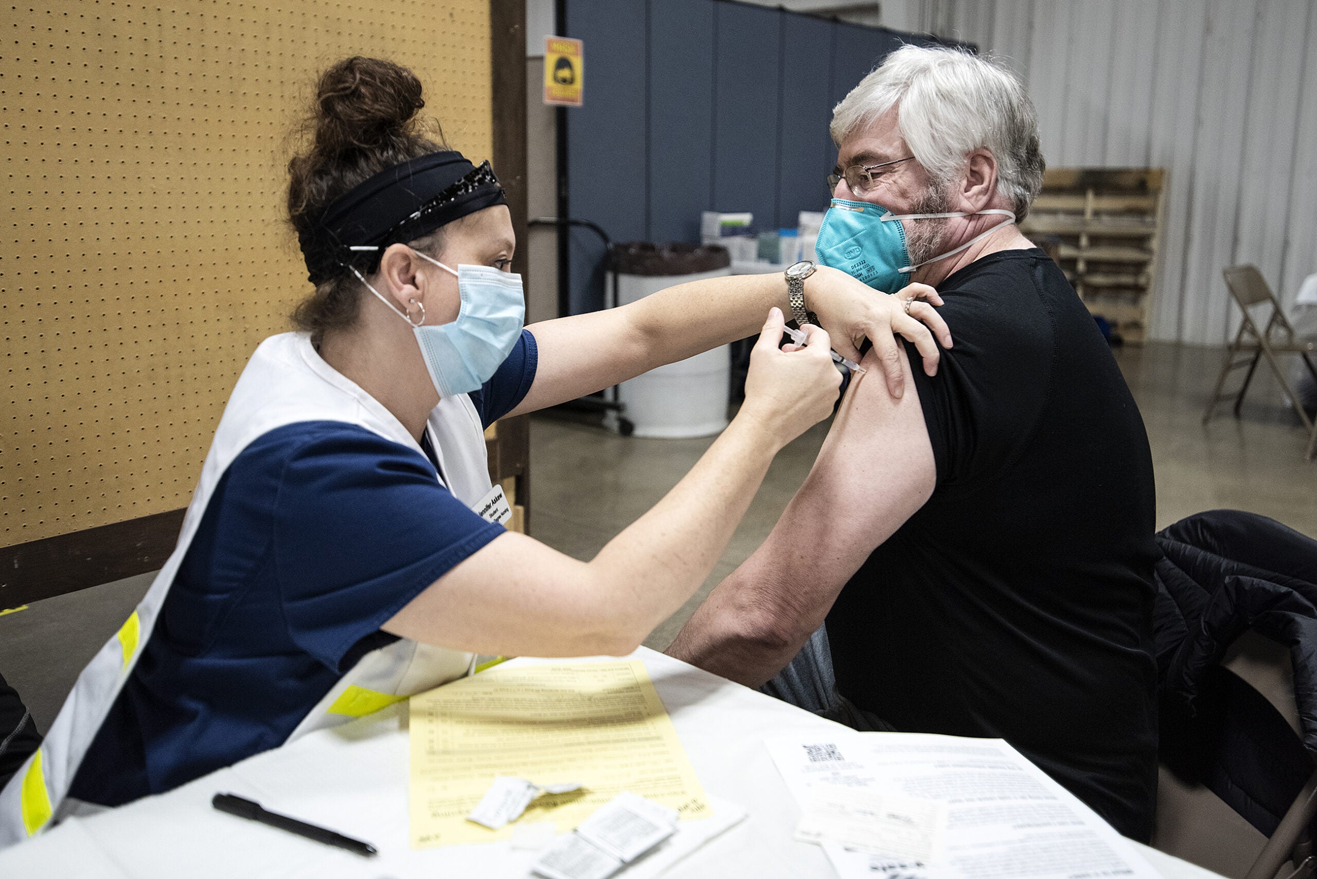 A nurse pulls up the sleeve of a man as she gives him a shot