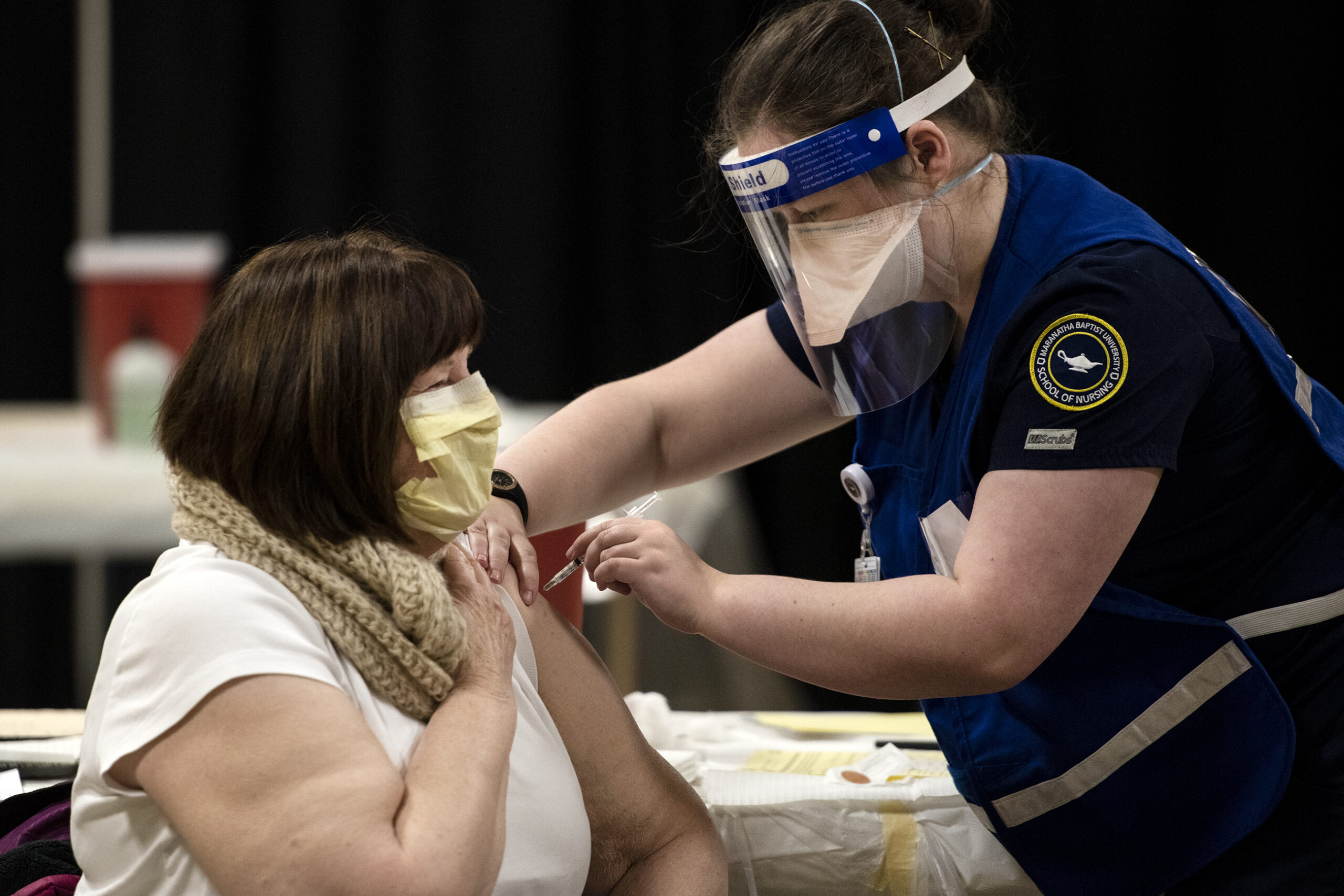 A woman in a face mask looks up at a nurse as she receives her covid-19 vaccine