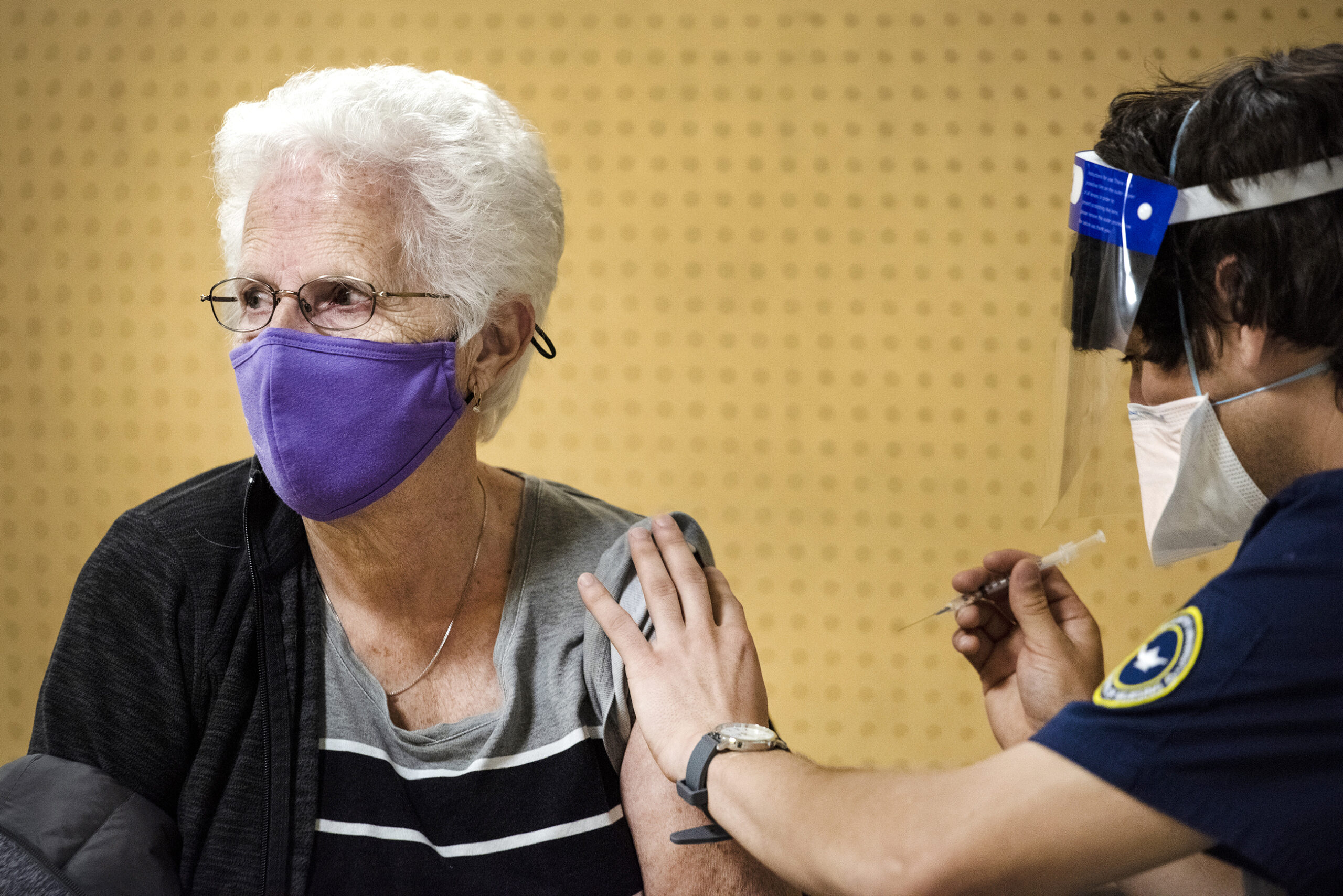 a woman in a purple face mask sits to receive her vaccine