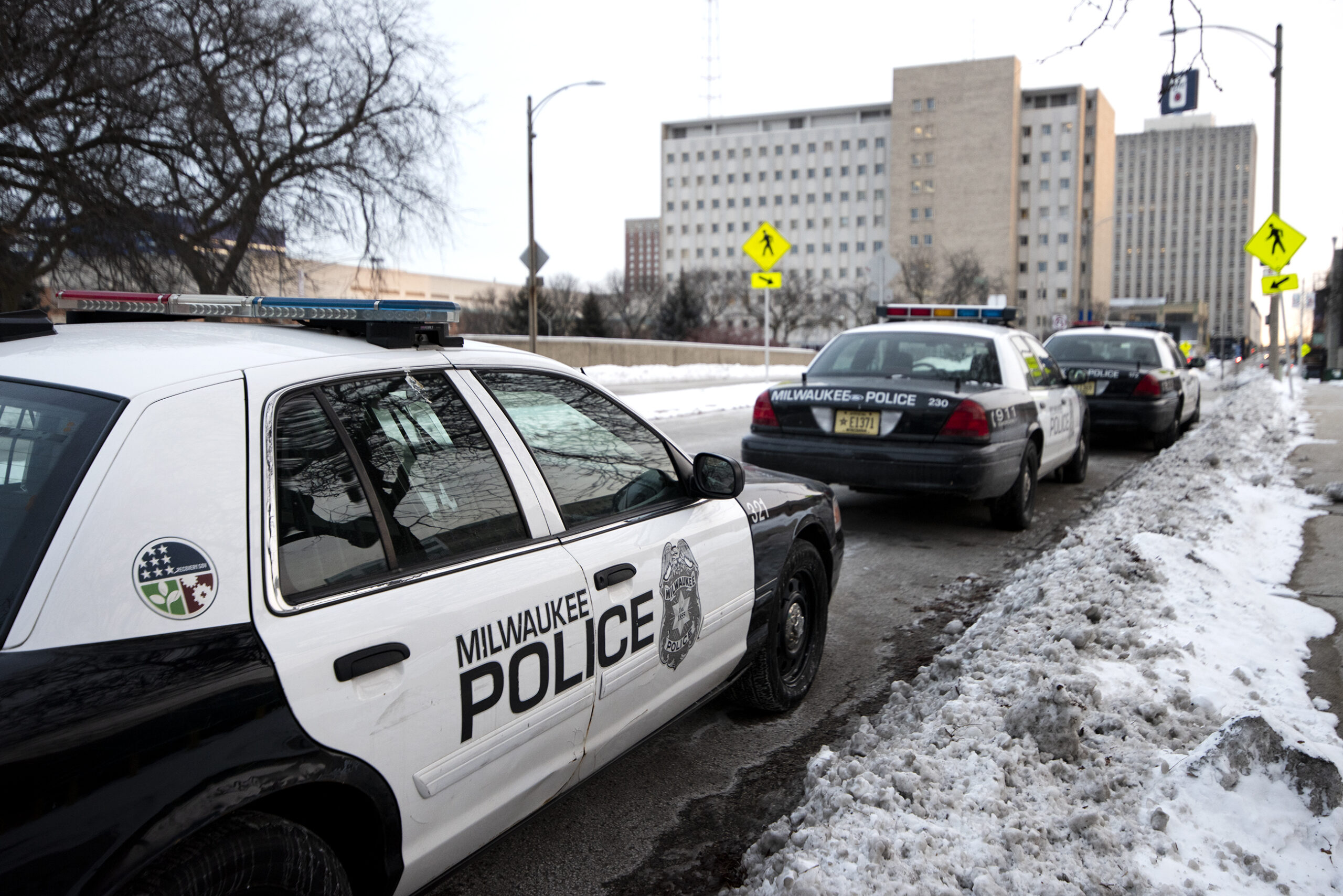 Three Milwaukee police cars are parked on a snowy street.