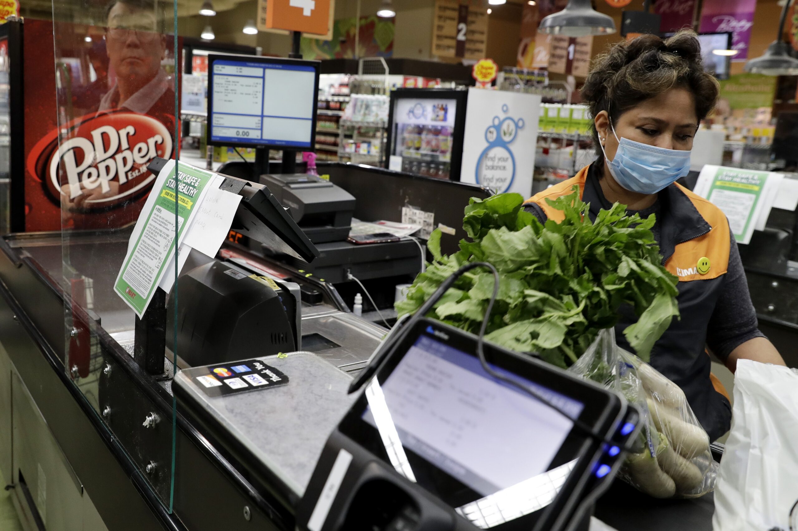 A cashier works behind a plexiglass shield at a Super H Mart grocery store